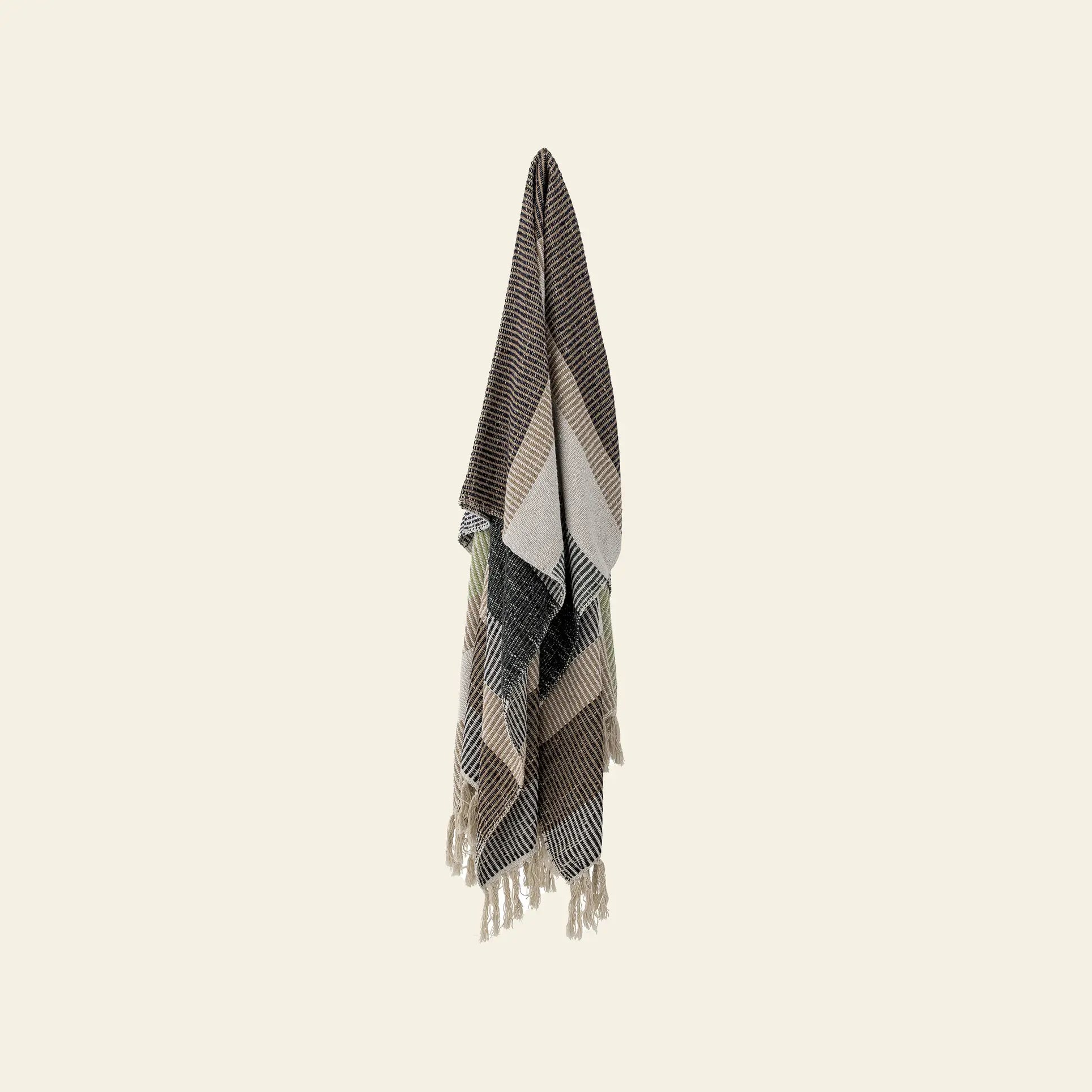 The Bloomingville Isnel Throw, made from recycled cotton, features stripes and chevron patterns in brown, black, cream, and taupe. Finished with tassels, this fringed blanket by Bloomingville adds texture and warmth to any light beige wall.