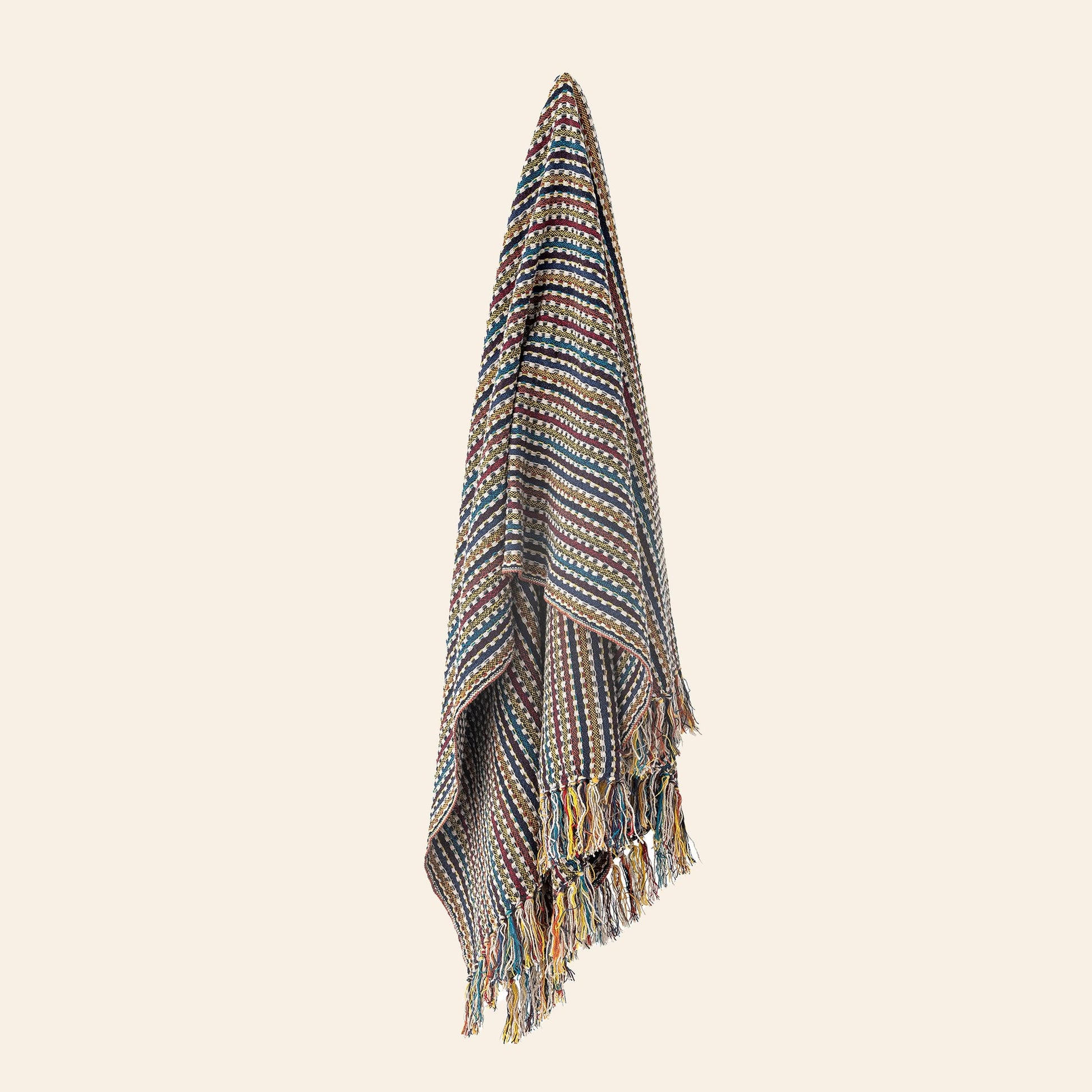 The Bloomingville Lazzario Throw by Bloomingville is a multicolored blanket with geometric stripes and fringed edges, shown hanging vertically against a plain, light background.