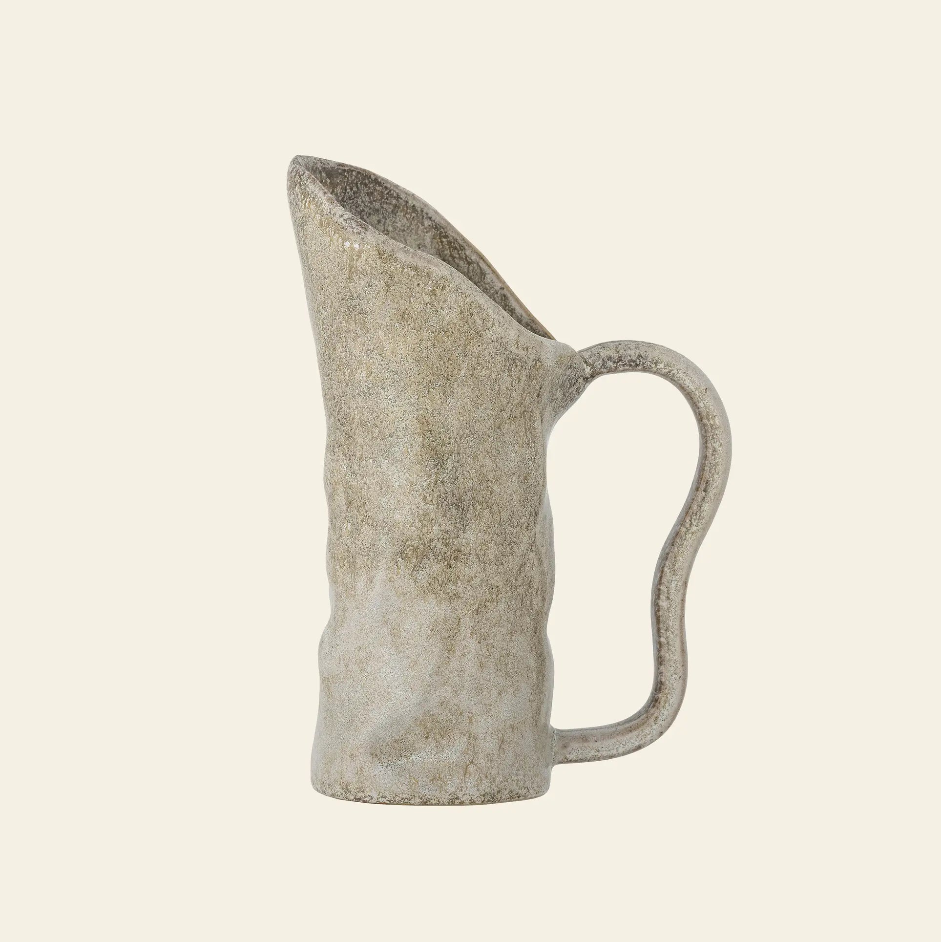 The Bloomingville Razan Jug from Bloomingville features a handmade, wavy surface and asymmetrical curved handle in an earthy, speckled beige finish—ideal as a decorative accent for any space.