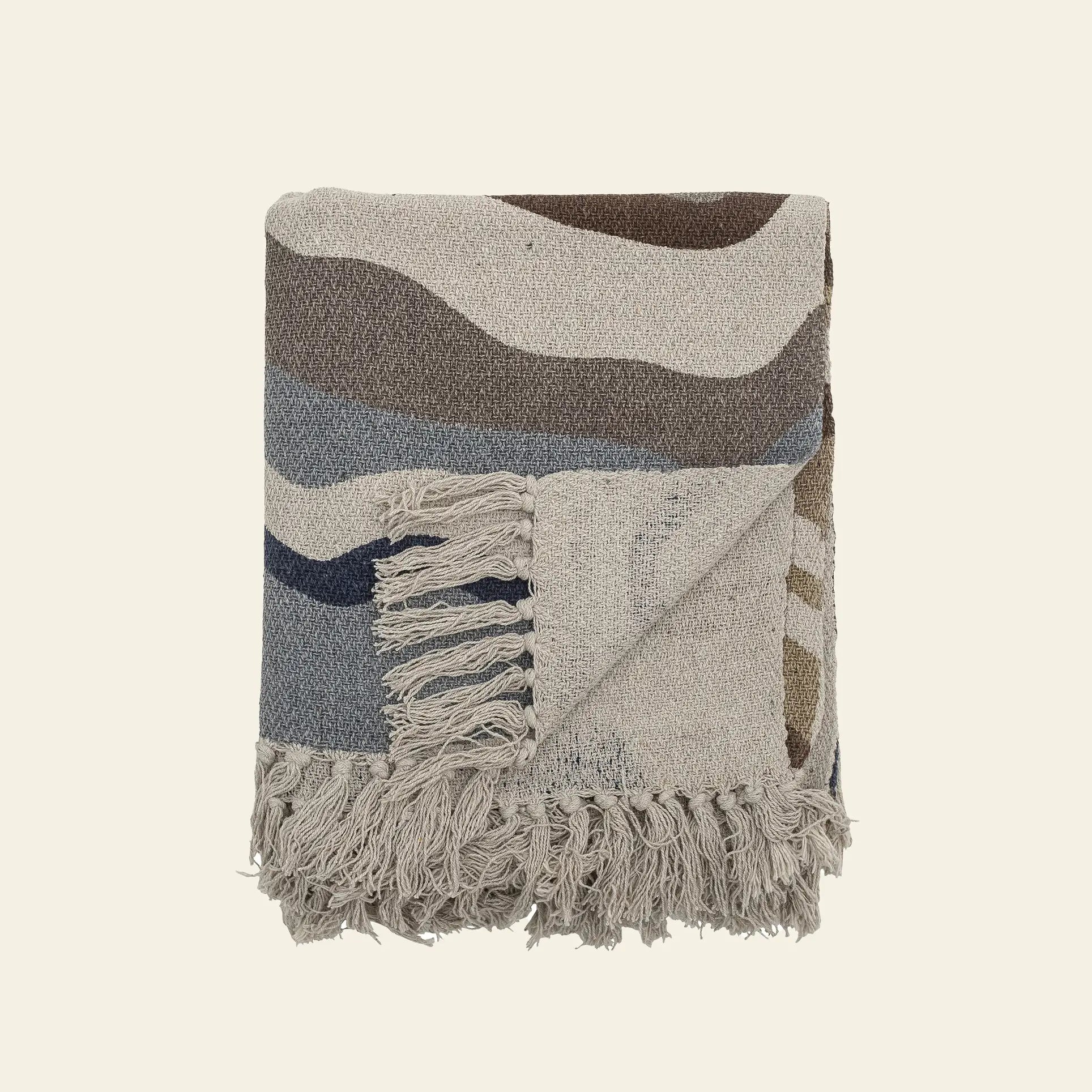 The Bloomingville Stephania Throw by Bloomingville is crafted from recycled cotton with abstract wavy patterns in beige, brown, blue, and gray. A turned-up corner displays tasseled fringe on two edges against a plain off-white background.