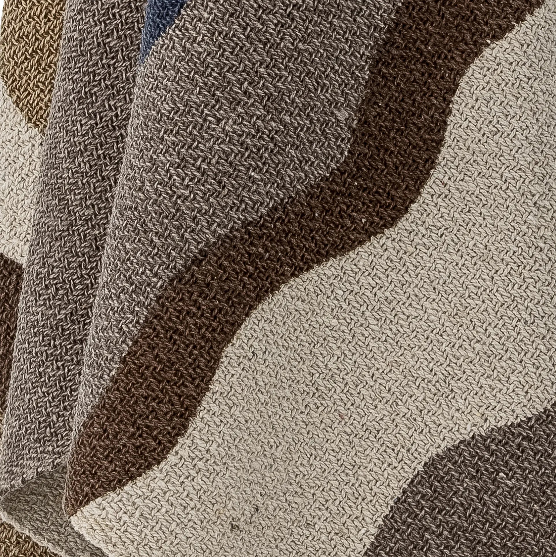 A close-up of the Bloomingville Stephania Throw by Bloomingville, showcasing its recycled cotton texture and woven wavy stripes in brown, beige, gray, and blue for a layered look.