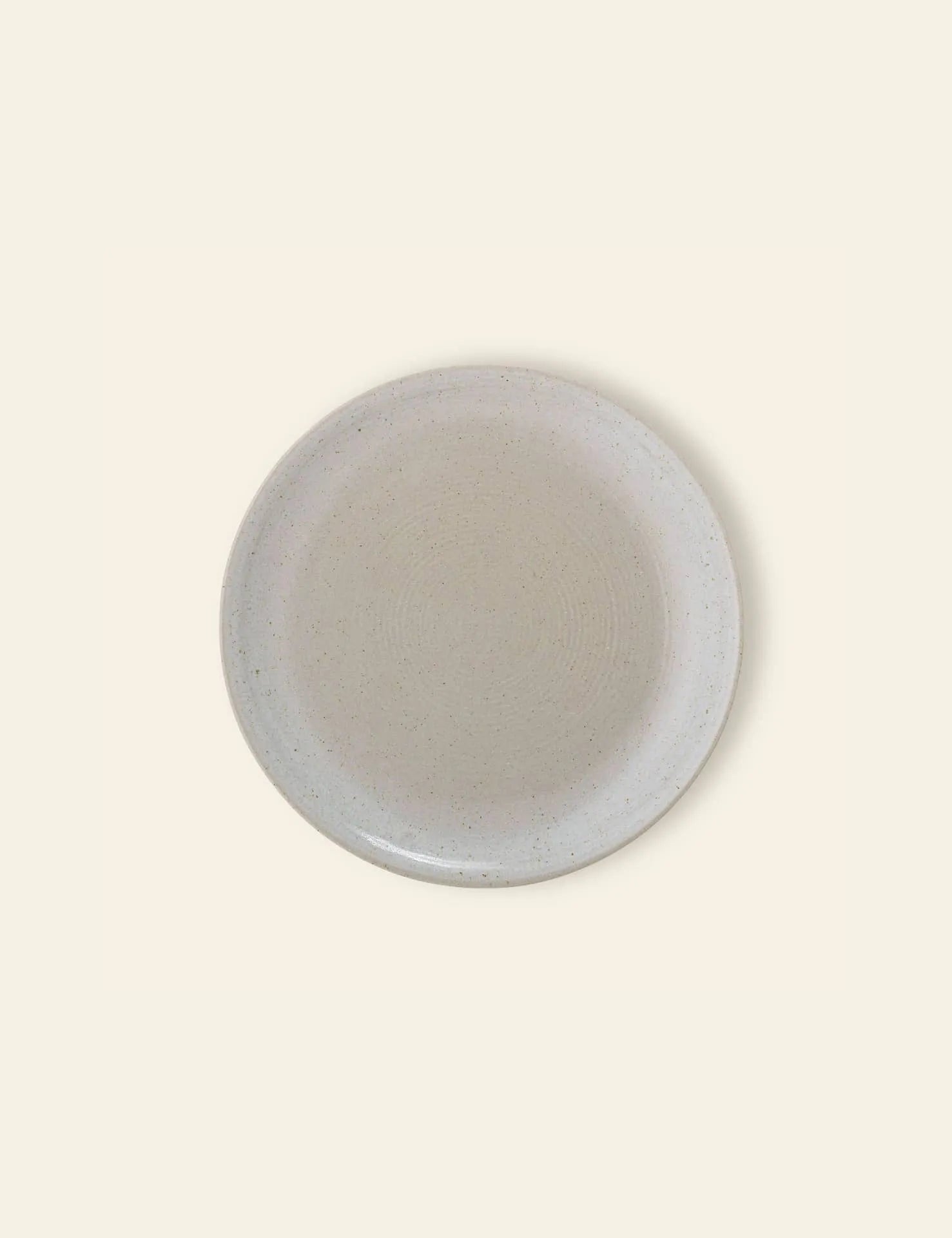The Bloomingville Taupe Plate by Bloomingville is a round stoneware plate in light beige with subtle speckled patterns, shown from above on a matching light background.