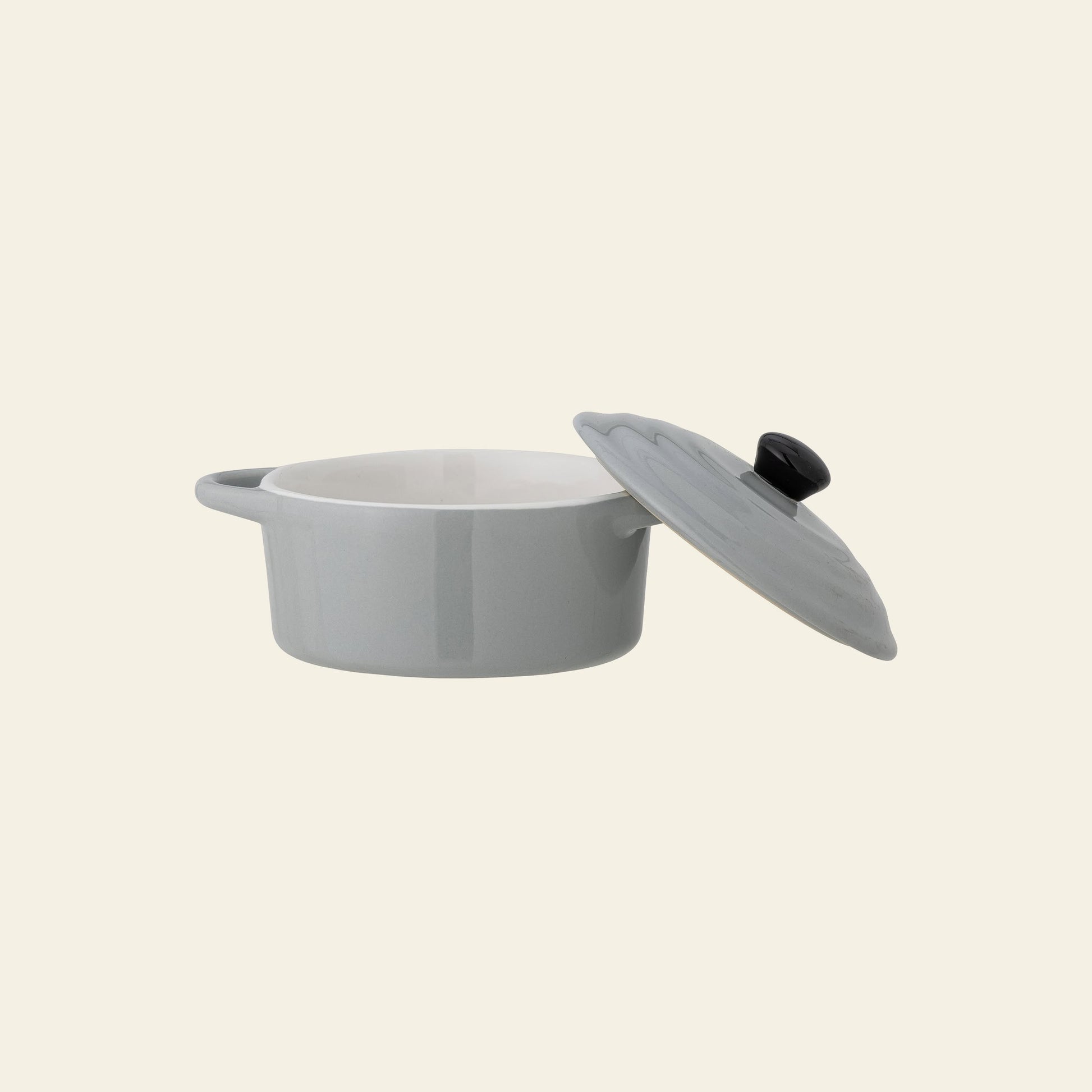 The Bloomingville Thanos Oven Dish w/Lid is a light gray stoneware casserole with a handle, shown with its lid slightly open against a plain beige background—ideal for casseroles and oven-to-table serving.