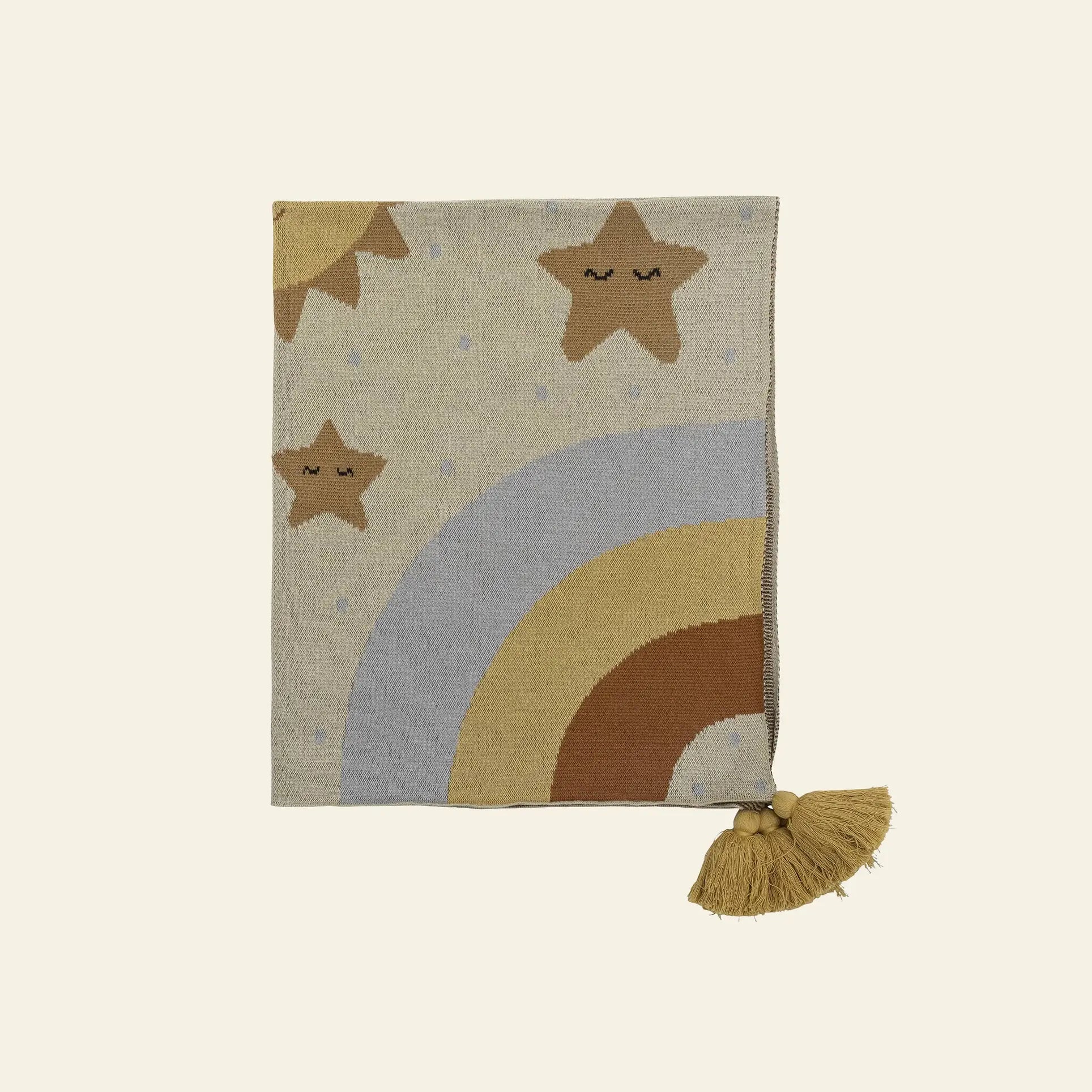 The Bloomingville Vigge Throw by Bloomingville is a sky-inspired knitted blanket with smiling stars, pastel rainbows in beige, blue, and brown, plus a tasseled corner with wooden beads. Made from OEKO-TEX certified cotton in cozy off-white.