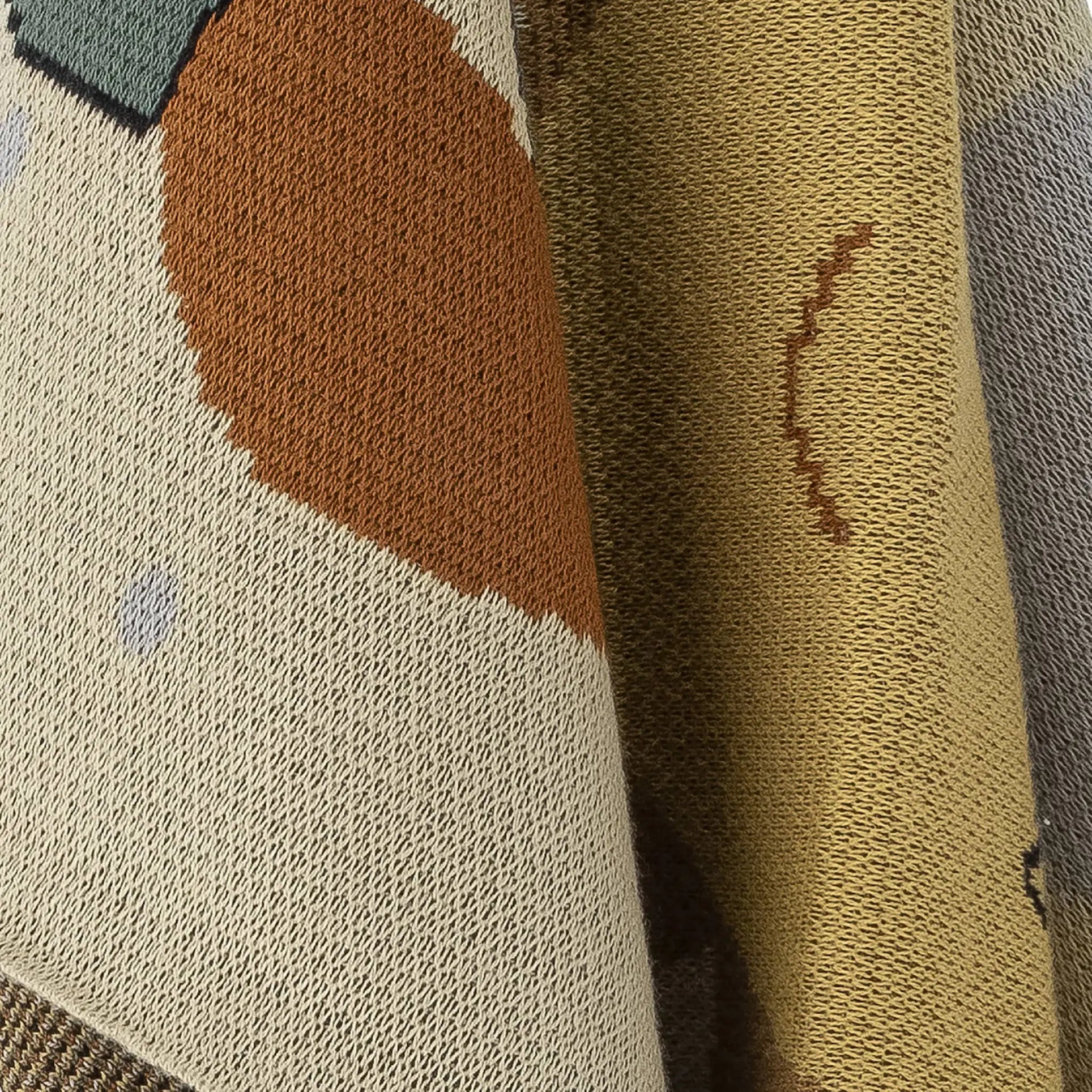 Close-up of the Bloomingville Vigge Throw by Bloomingville, a knitted blanket with abstract sky-themed patterns in tan, brown, beige, light blue, and yellow OEKO-TEX certified cotton. Features textured stitches and layered designs.