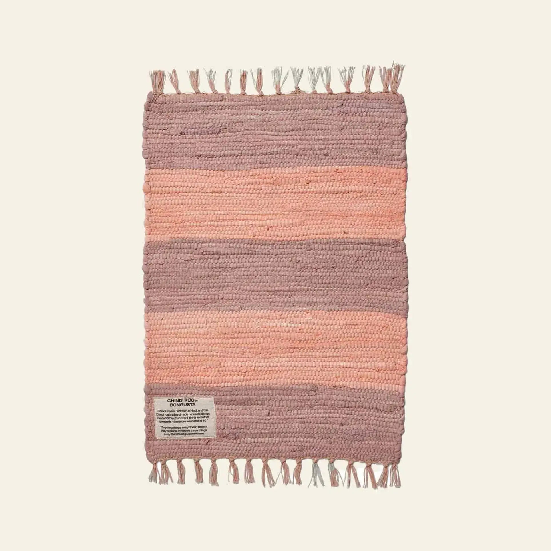 The Bongusta Chindi Rug (45x60) is handcrafted in India from surplus cotton with pink horizontal bands, off-white background, and fringe on the short ends. A small fabric label accents one corner. Brand: Bongusta.