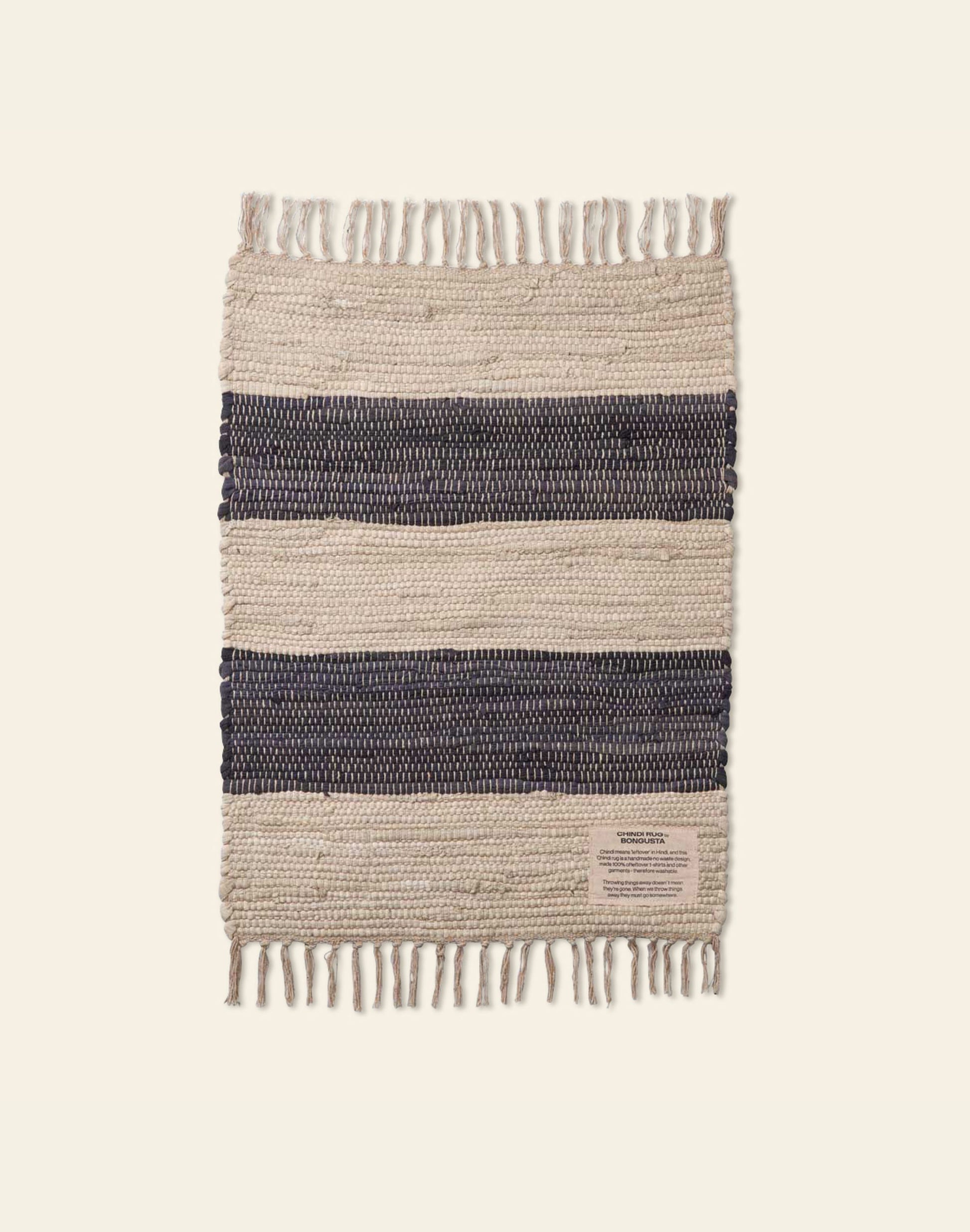 The Bongusta Chindi Rug (45x60) by Bongusta is a rectangular, handcrafted Indian rug with fringed edges, alternating cream and dark navy blue stripes, made from surplus cotton and finished with a small beige label on one corner.