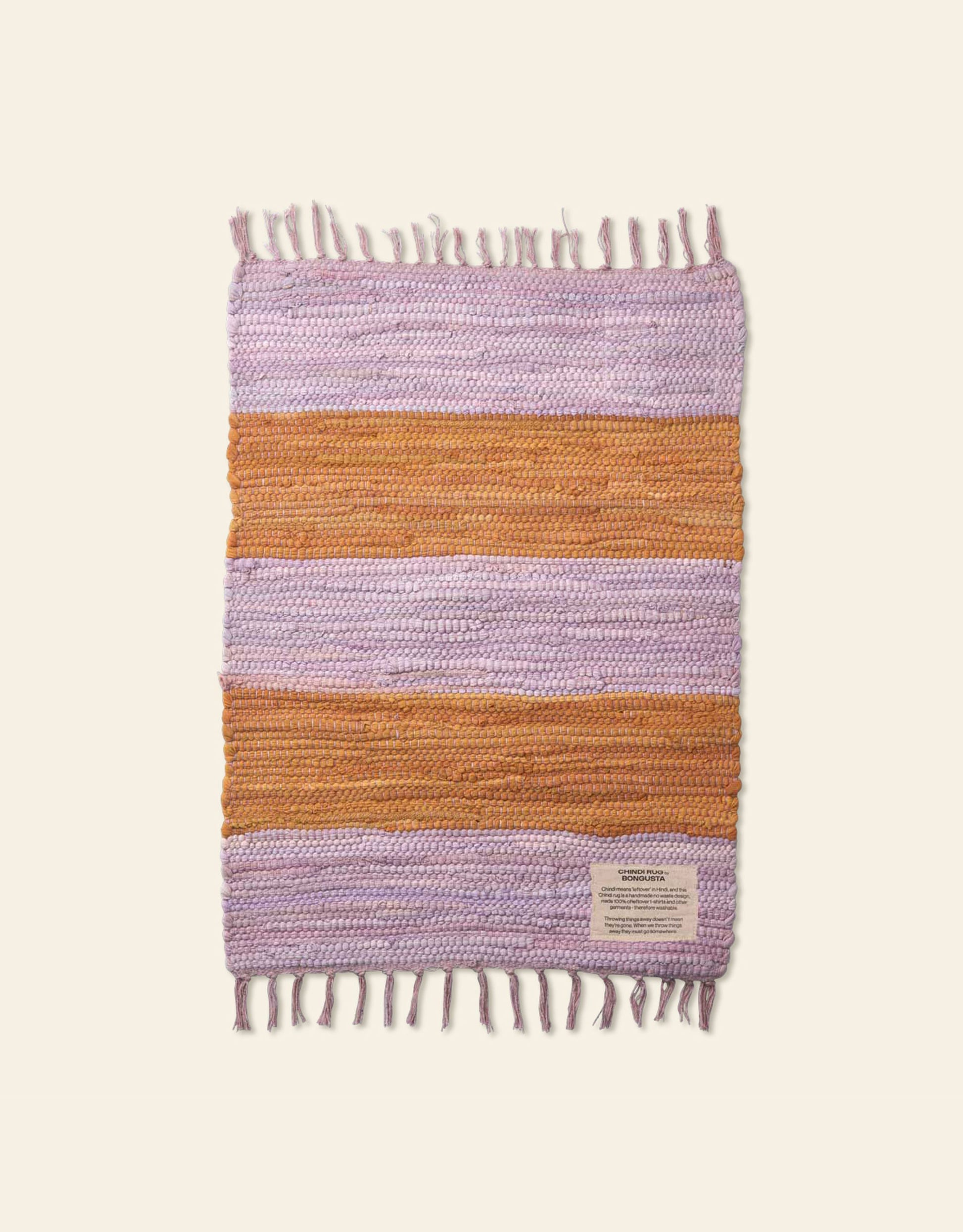 The Bongusta Chindi Rug (45x60) by Bongusta is handcrafted in India from surplus cotton with off-white, lavender, and orange horizontal stripes, short fringe ends, and a rectangular corner label.