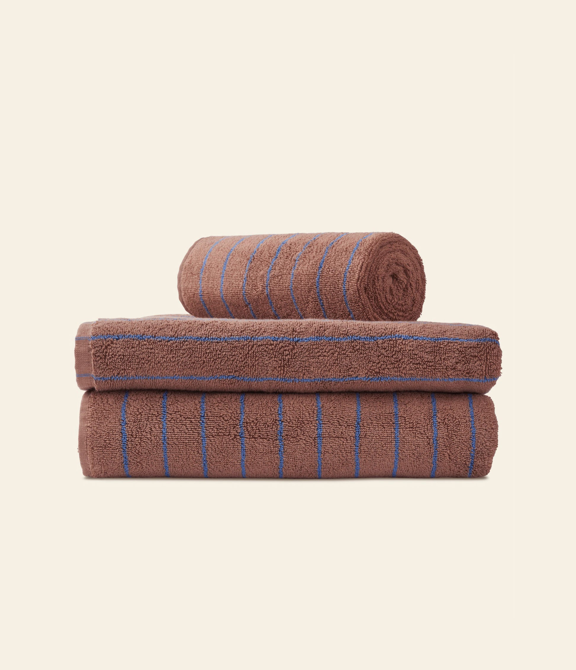 Three brown Bongusta Naram Bath Towels with thin blue stripes are stacked neatly against a light background. Made from Oeko-Tex combed cotton, one luxury towel is rolled on top of two folded towels by Bongusta.
