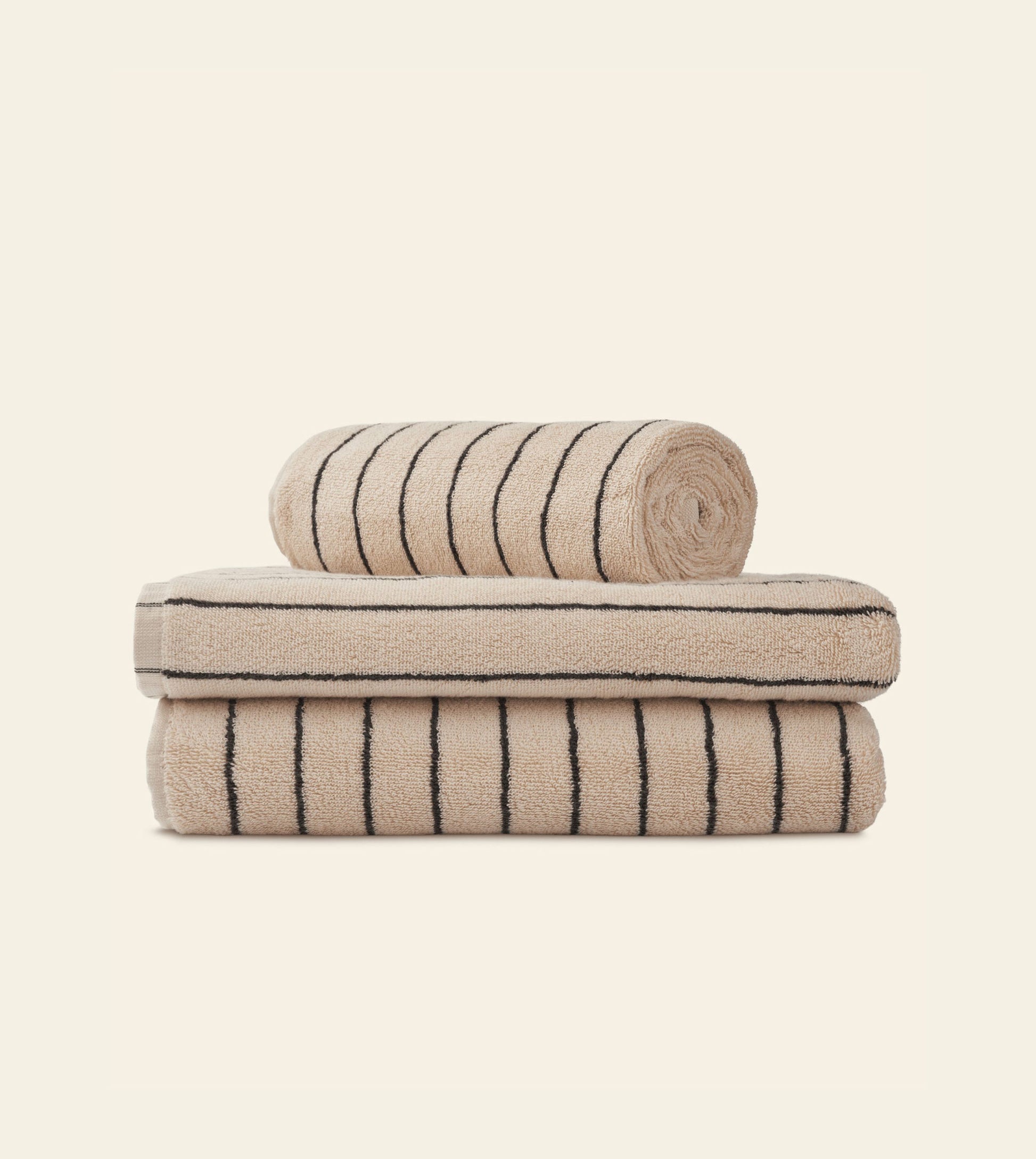 Three Bongusta Naram Bath Towels in beige with black stripes—made from Oeko-Tex combed cotton—are stacked against a light backdrop, with two folded and one rolled on top, showcasing the luxury and quality of Bongusta.