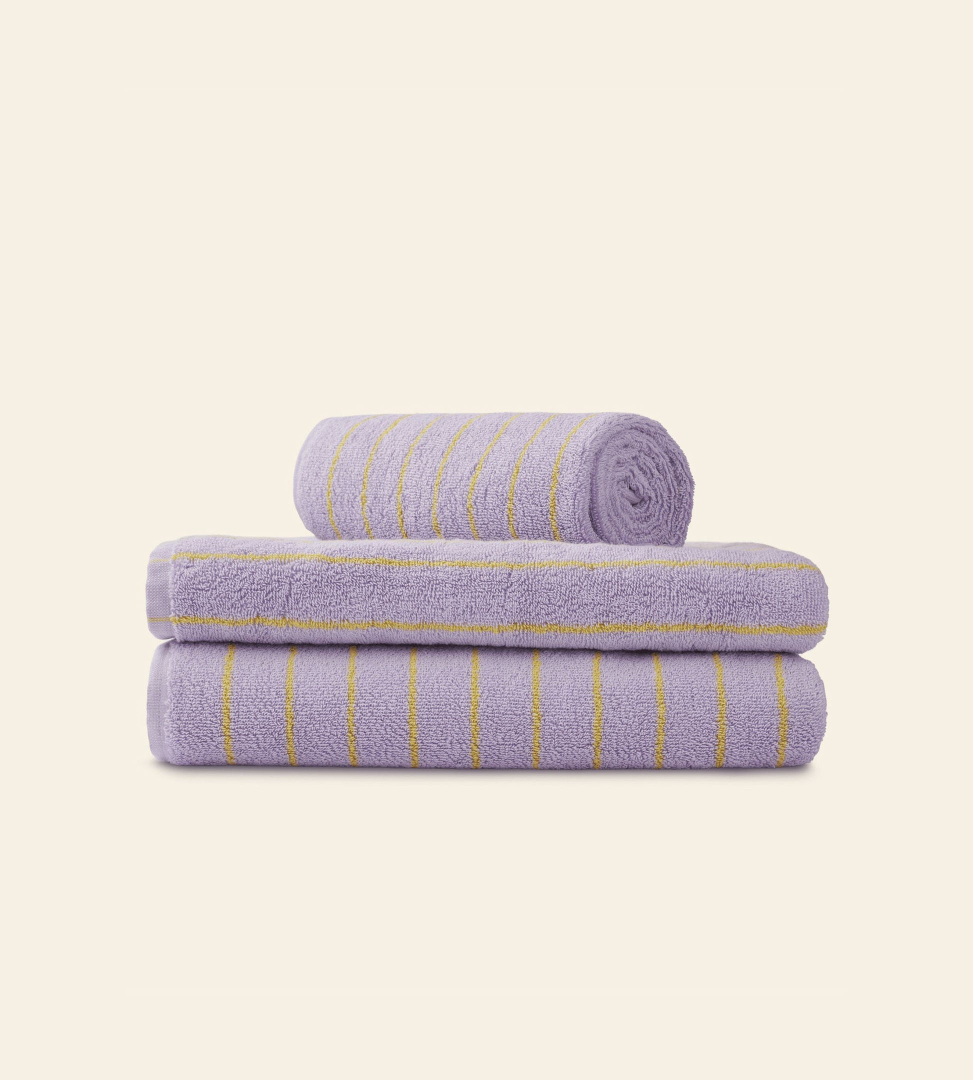Three folded Bongusta Naram Bath Towels in lavender with yellow stripes, made from Oeko-Tex combed cotton, are stacked on a light beige background—two flat and one rolled on top—highlighting Bongustas luxury.