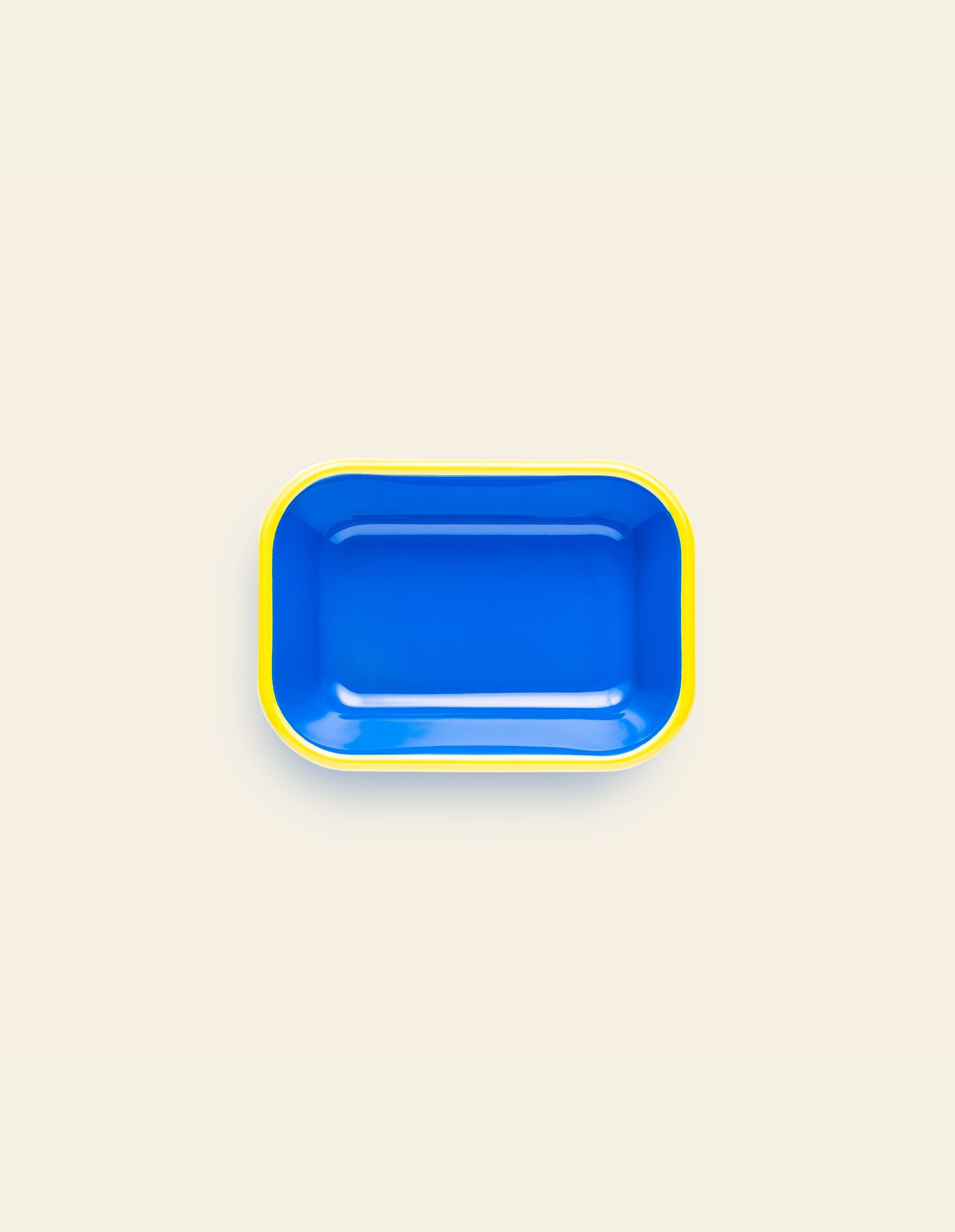 The Bornn Enamelware Colorama Baking Dish, Small, by Bornn Enamelware, is a rectangular blue tray with rounded corners and a yellow rim, handmade and shown on a light beige background.