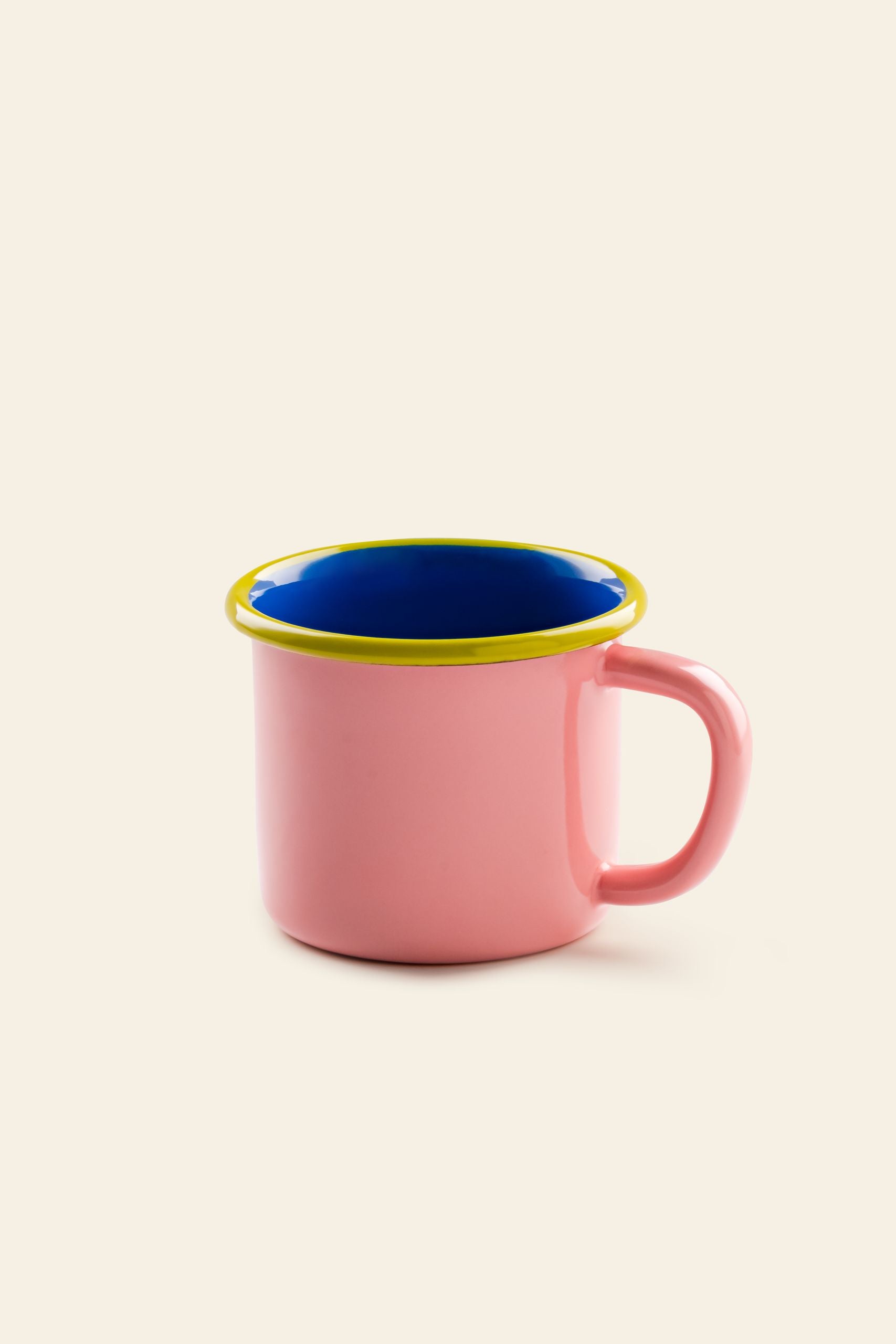 The Bornn Enamelware Colorama Mug by Bornn Enamelware features a pink enamel finish, large handle, yellow rim, and deep blue interior, displayed against a plain light beige background.