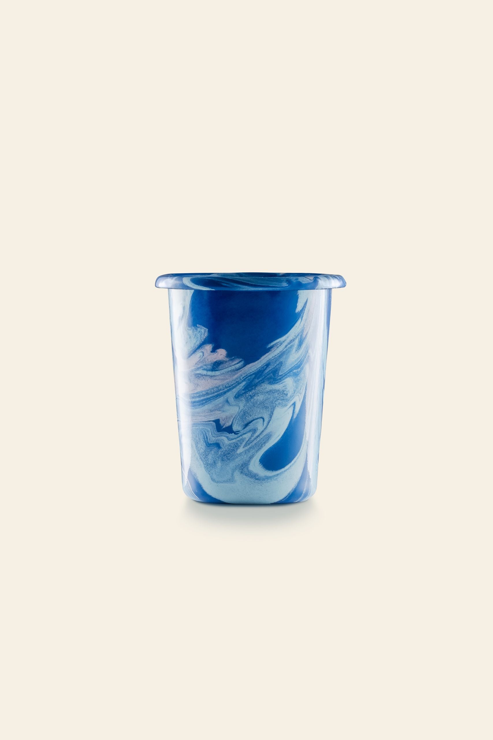 A small glass cup with swirling blue and white marbled patterns, inspired by the Bornn Enamelware New Marble Tumbler Cup, is set against a plain, light beige background.