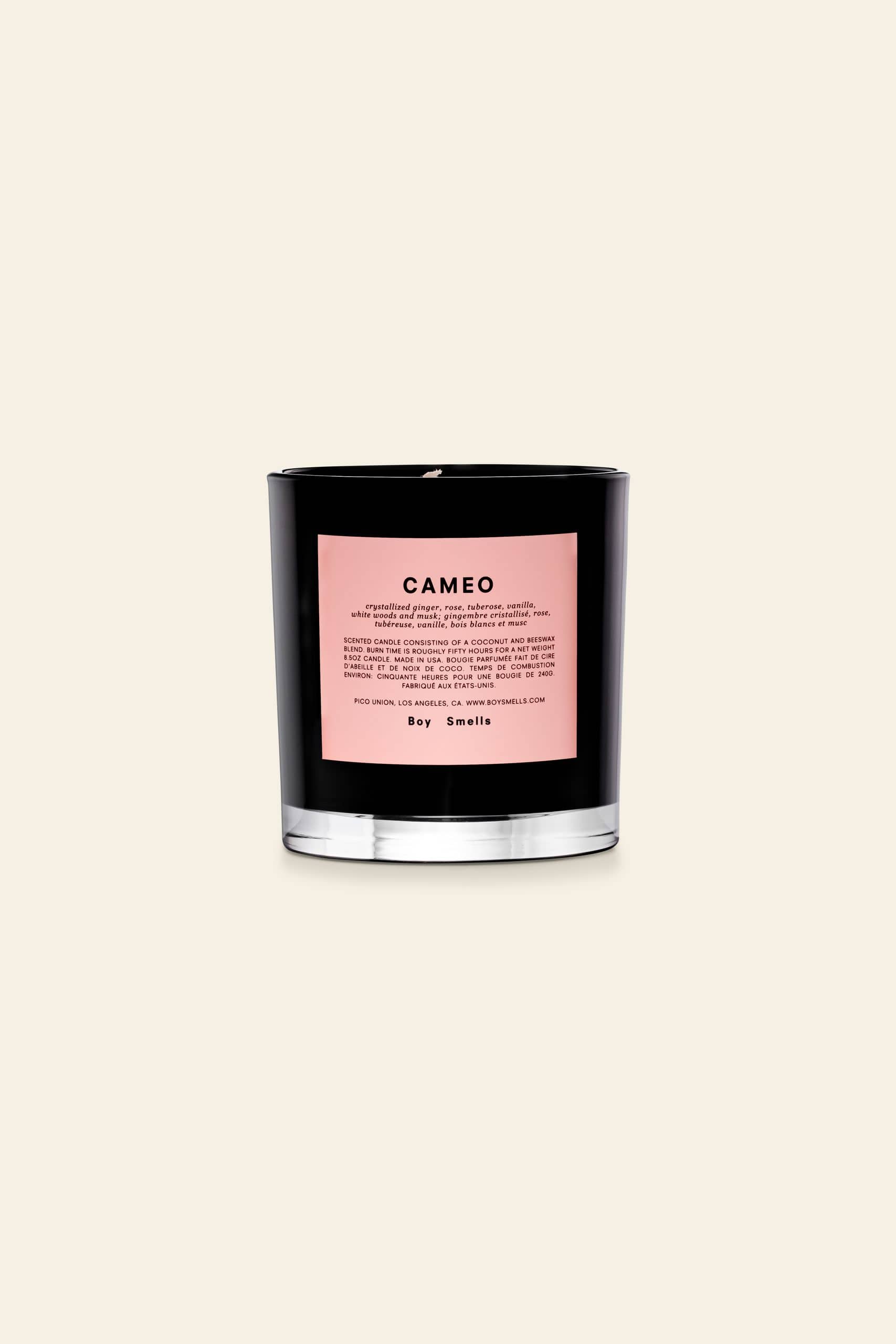 The Boy Smells Cameo Scented Candle 8.5oz features a black glass jar with a pink label marked CAMEO, listing notes like crystallised ginger. It rests on a beige background, with the Boy Smells brand at the bottom of the label.