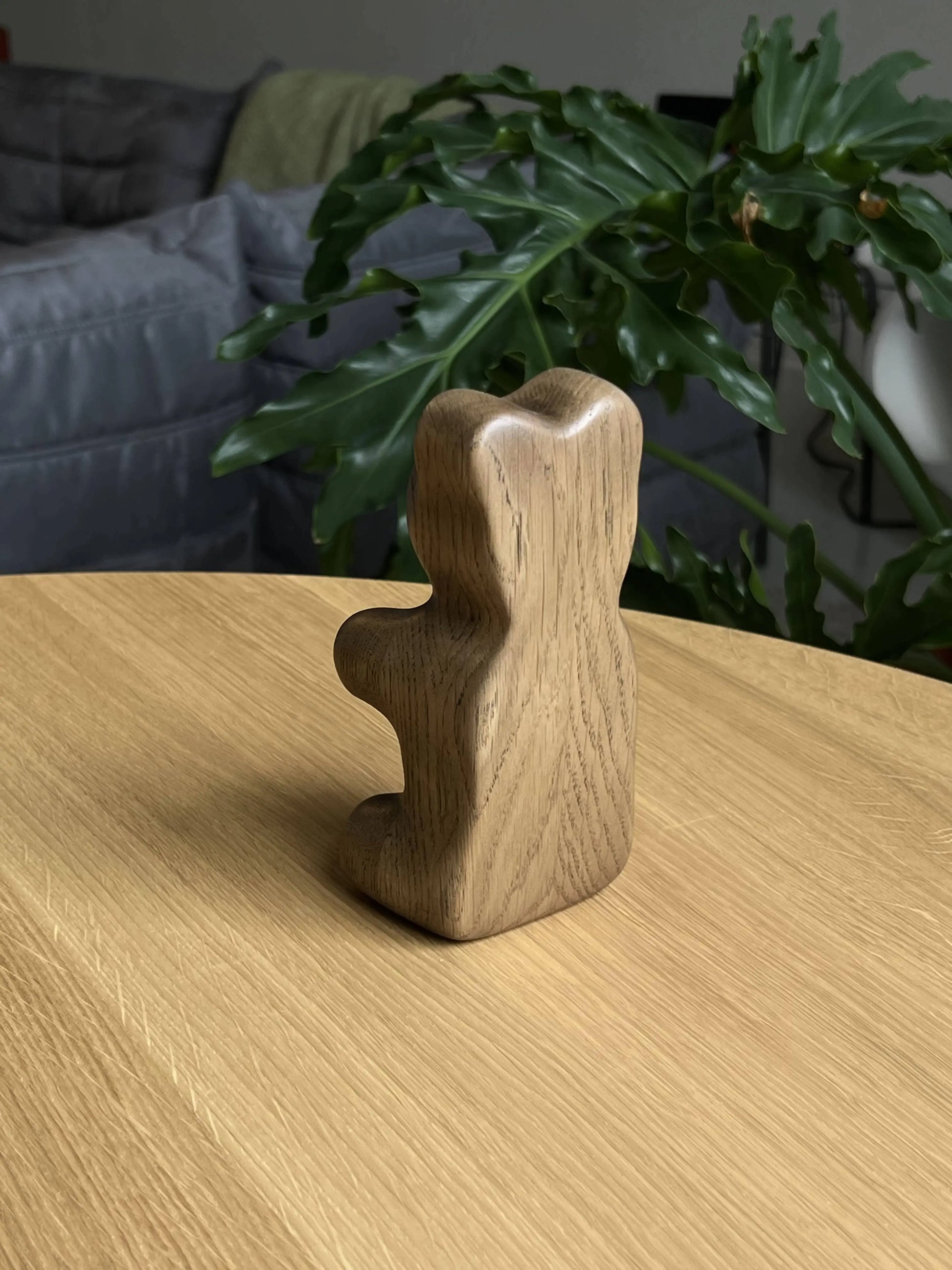 The Boyhood Gummy Bear Small by Boyhood stands upright on a light wooden table, eye-catching against a softly blurred background with a green leafy plant and gray couch.