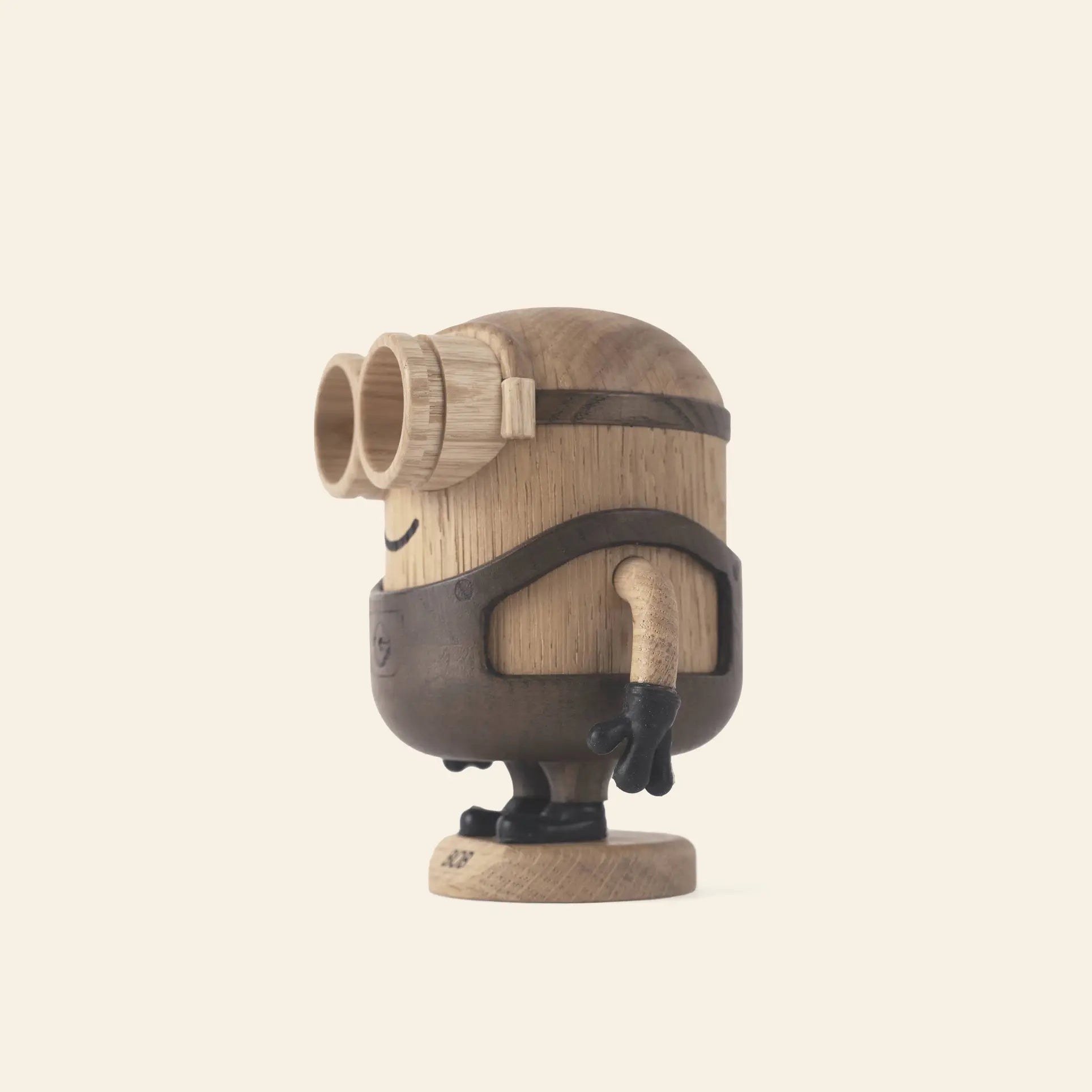 The Boyhood Minion Bob Small by Boyhood is a wooden figurine inspired by the Minions movies, featuring large goggles, black gloves, and an overall outfit crafted from various wood tones. It stands playfully against a light background.