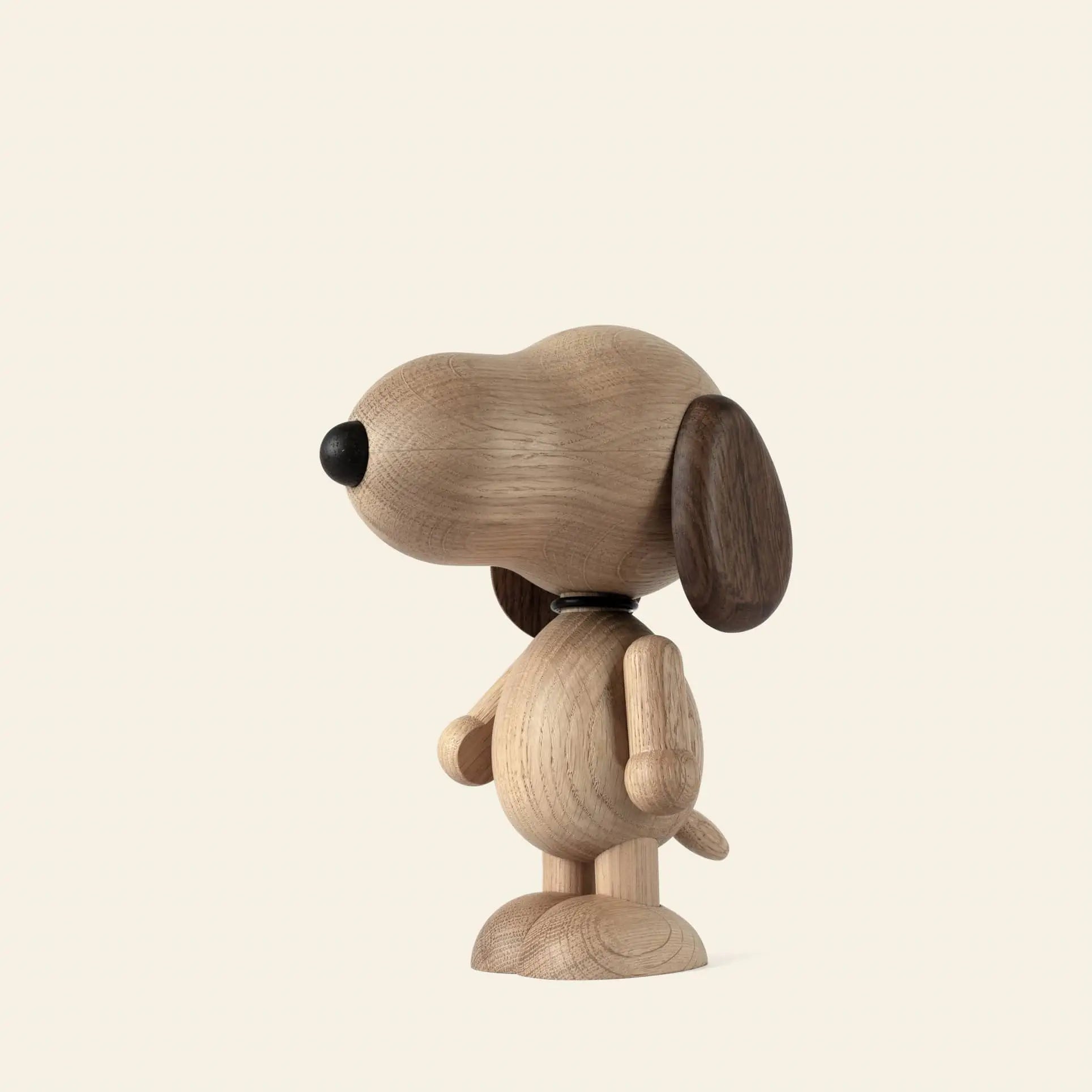 The Boyhood Snoopy Small by Boyhood is a wooden figurine of Snoopy with smooth natural wood, dark wood ears, and a black nose. It stands upright facing left against a plain off-white background.