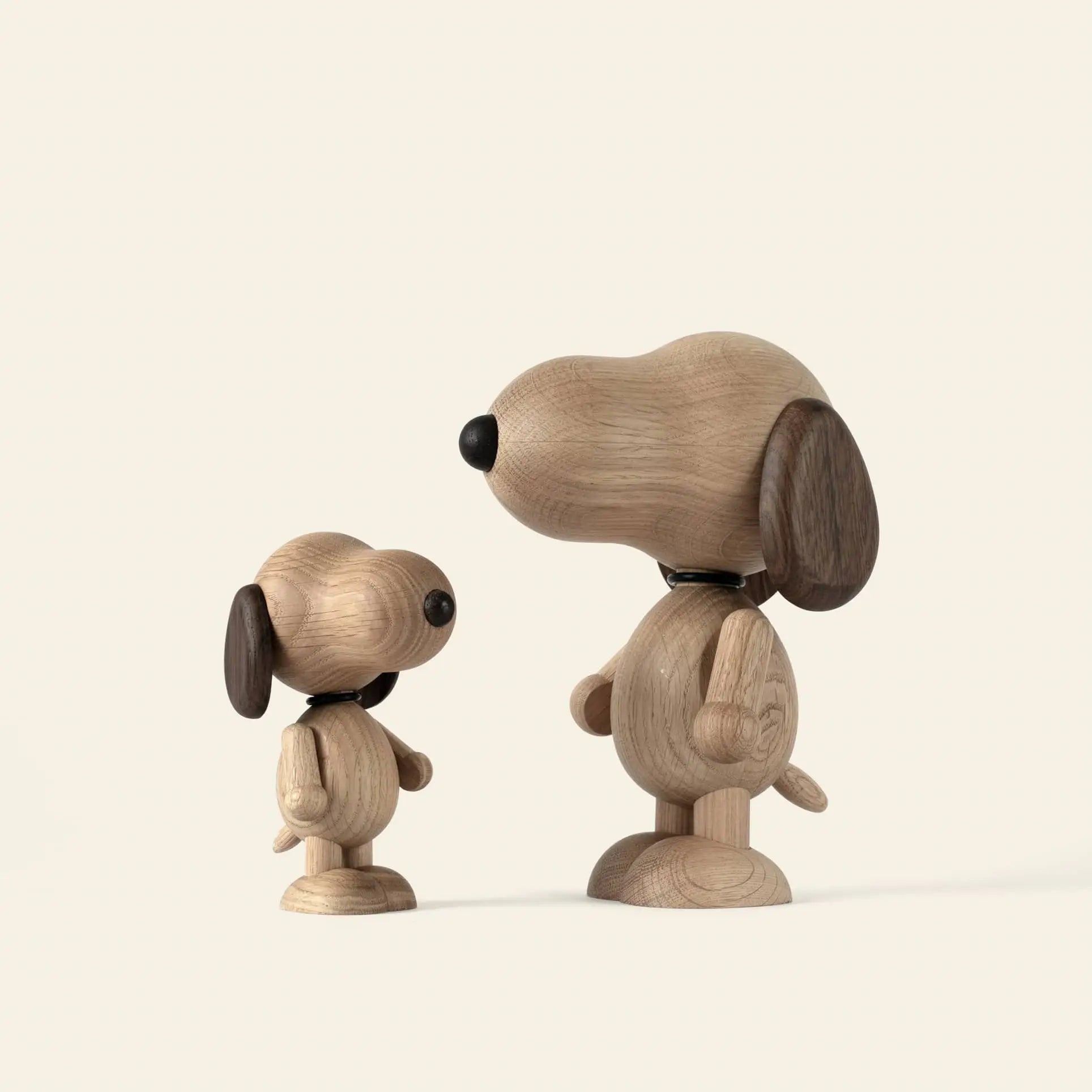 Two Boyhood Snoopy Small wooden dog figurines from Boyhood, one large and one small, stand facing each other on a light background. Their rounded shapes, dark brown ears, and black noses evoke the classic Charlie Brown character.