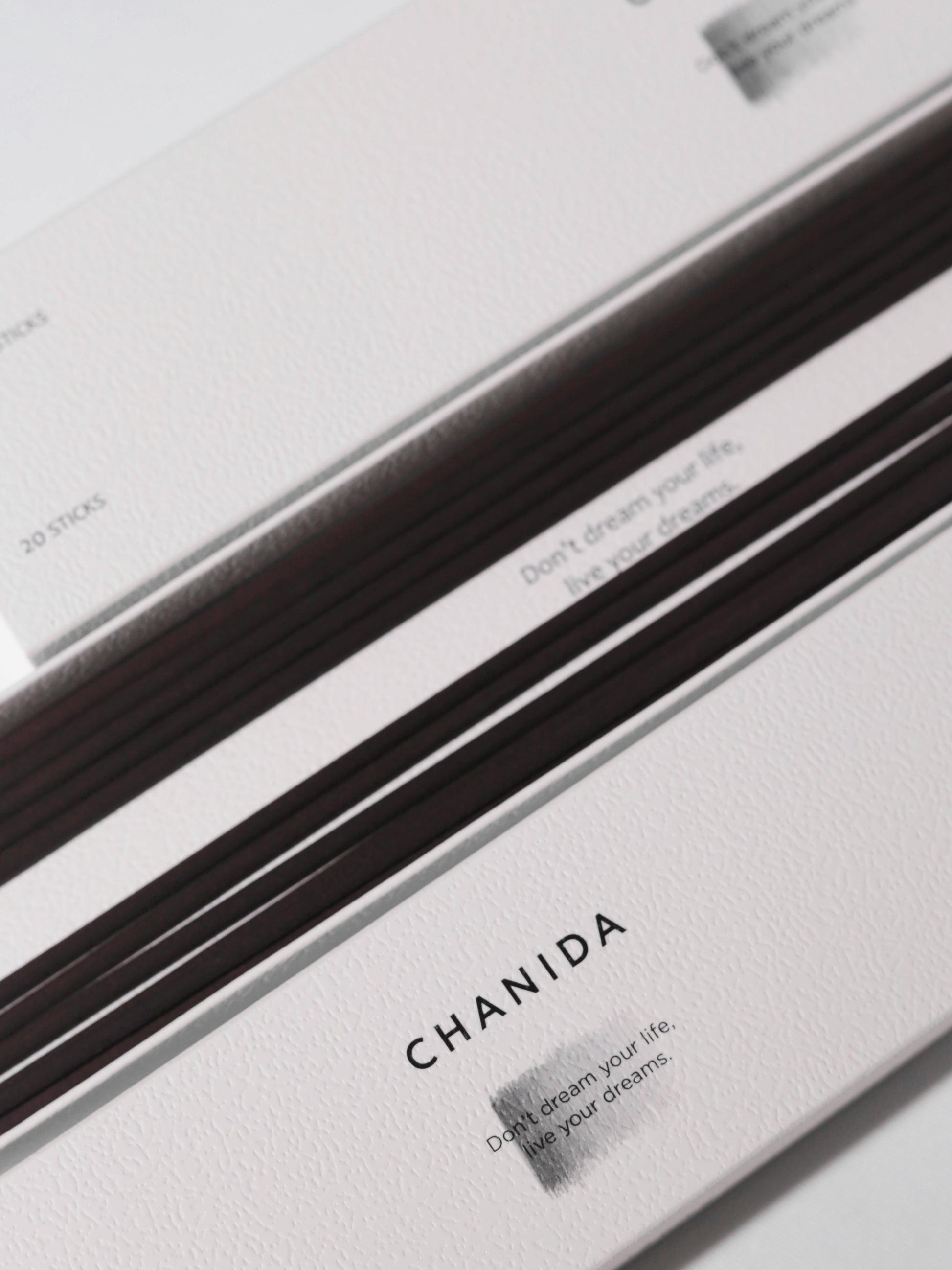 A close-up of CHANIDA Guaiacwood-Sandalwood Incense Sticks packaging shows thin brown incense sticks and the slogan “Don’t dream your life, live your dreams” on a textured white box.