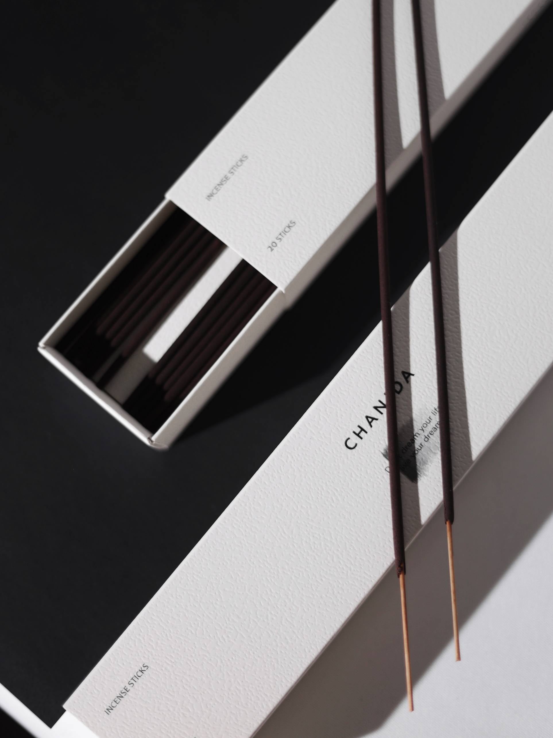 Two open white boxes labeled CHANIDA hold Hinoki-Rose Incense Sticks—ideal for meditation or adding a subtle rose-wood scent—presented on a bold black and white background.