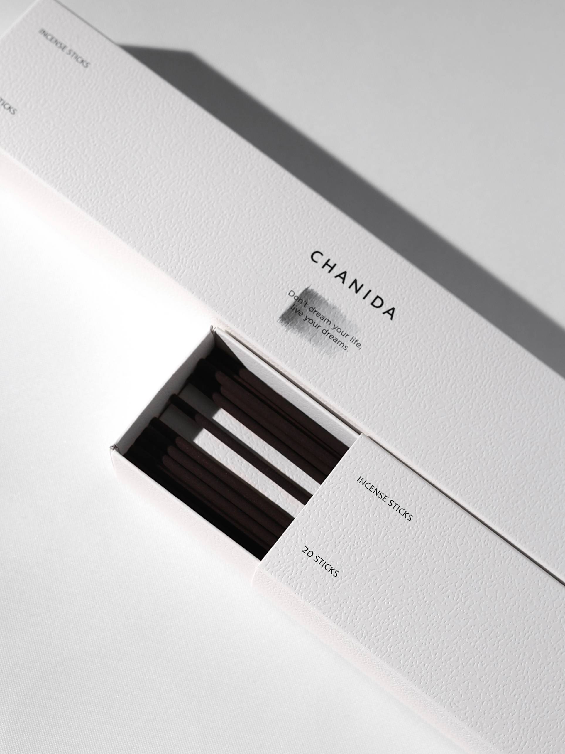 A white textured CHANIDA box labeled Lavender-Musk Incense Sticks is partially open, revealing several dark sticks inside. The box notes 20 sticks and soothing lavender hints, resting on a white surface with soft shadows.