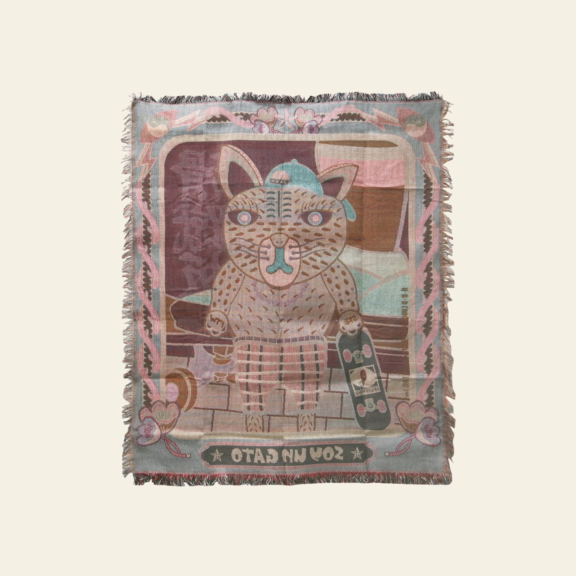 The DETAIL Black Cat Oax Throwket by DETAIL features a stylized black cartoon cat with brown stripes, wearing a beanie, holding a skateboard on brickwork. This multicolour throw blanket has pastel borders and “Soy Un Gato” at the bottom.