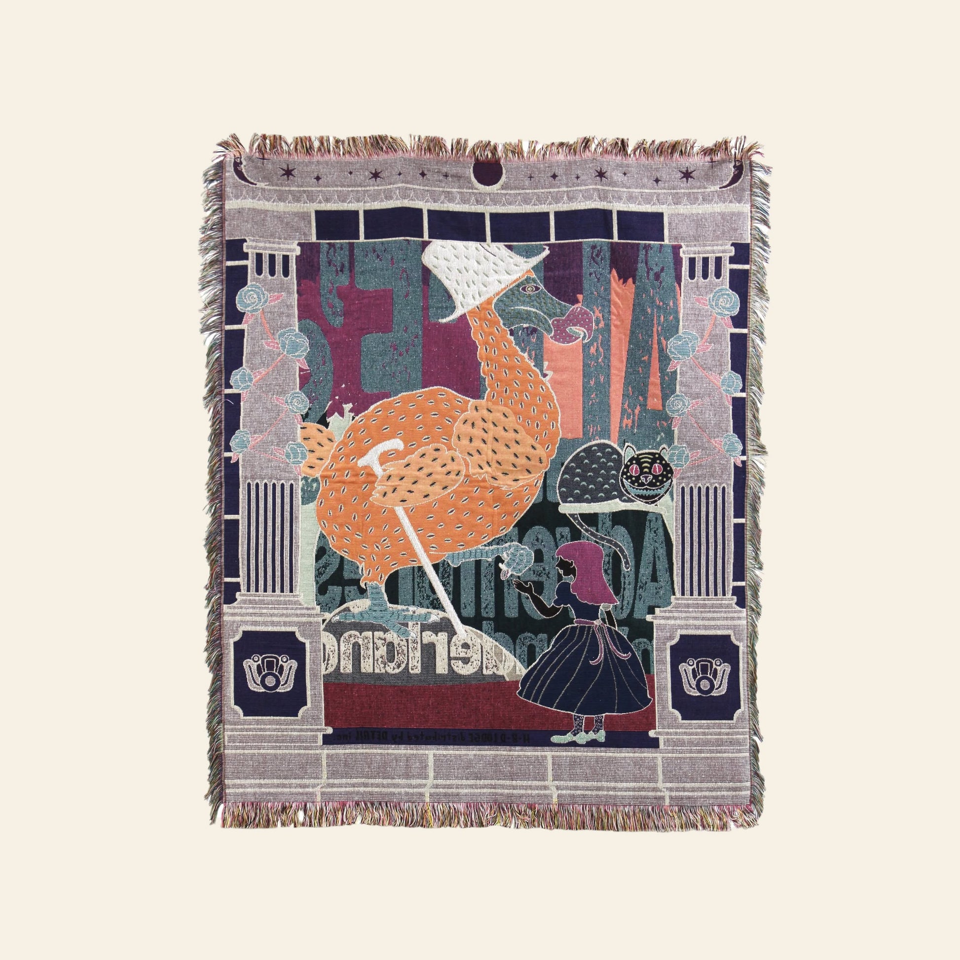 The DETAIL Dodo Oax Throwket by DETAIL is a folk art woven tapestry featuring a large orange bird in a bonnet with an umbrella, beside a girl and grinning cat amid stone pillars—an Alice in Wonderland-inspired throw blanket.