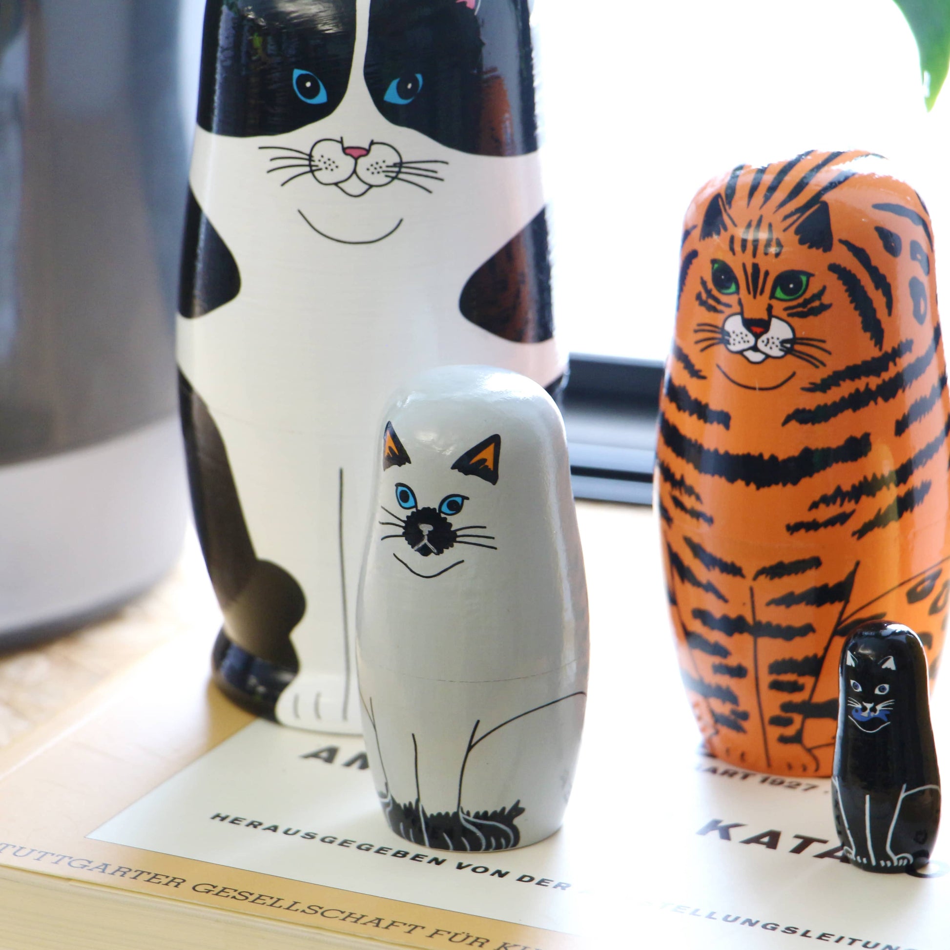 The DETAIL Feline 5 Nesting Dolls by DETAIL features five wooden cats, each with distinct fur patterns—black and white, orange, gray, and black—perfect for cat lovers to display near a sunny window.