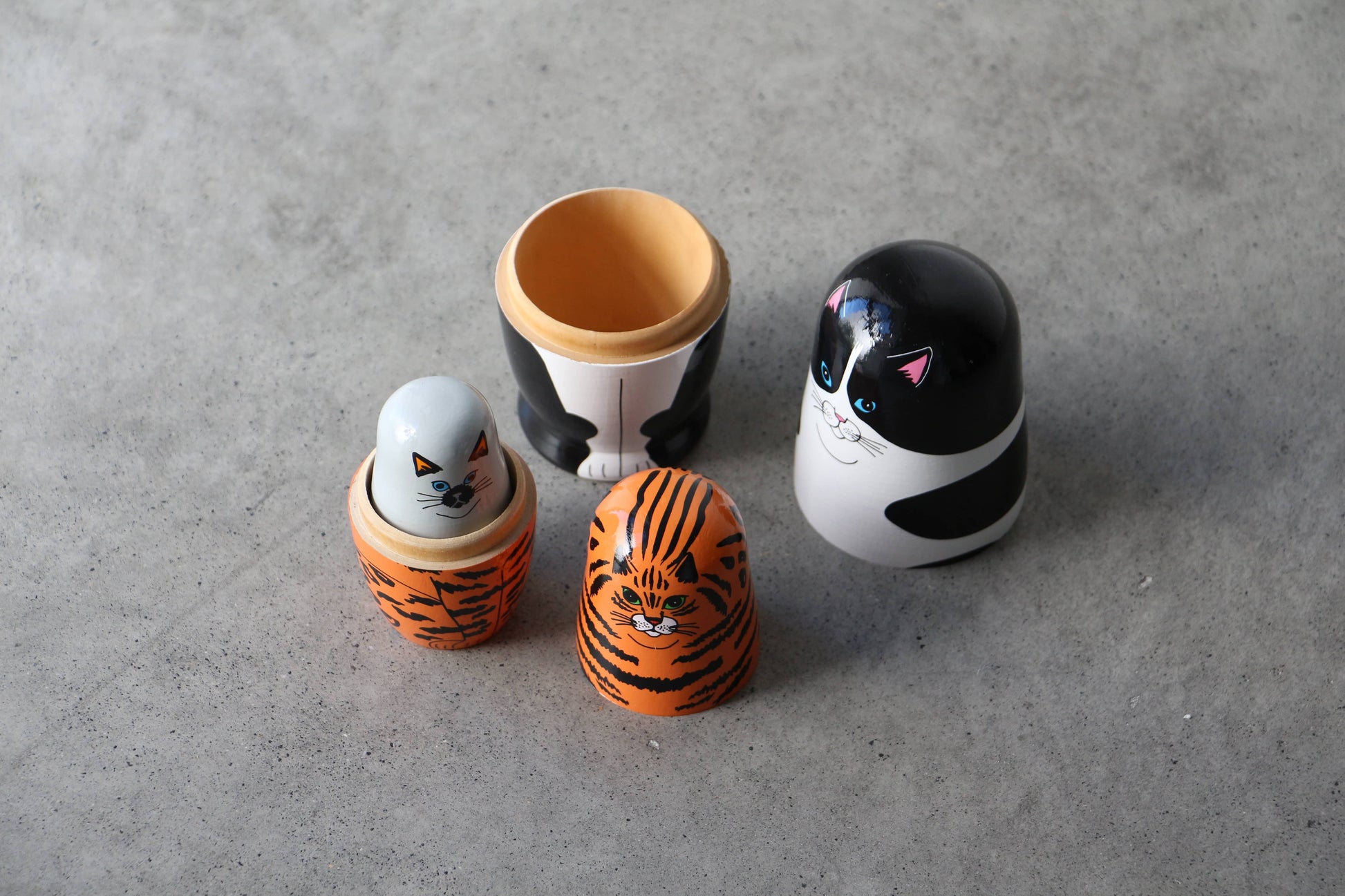 The DETAIL Feline 5 Nesting Dolls by DETAIL, featuring cat designs including a tiger-striped one, are shown open on a gray surface with their inner dolls displayed beside them.