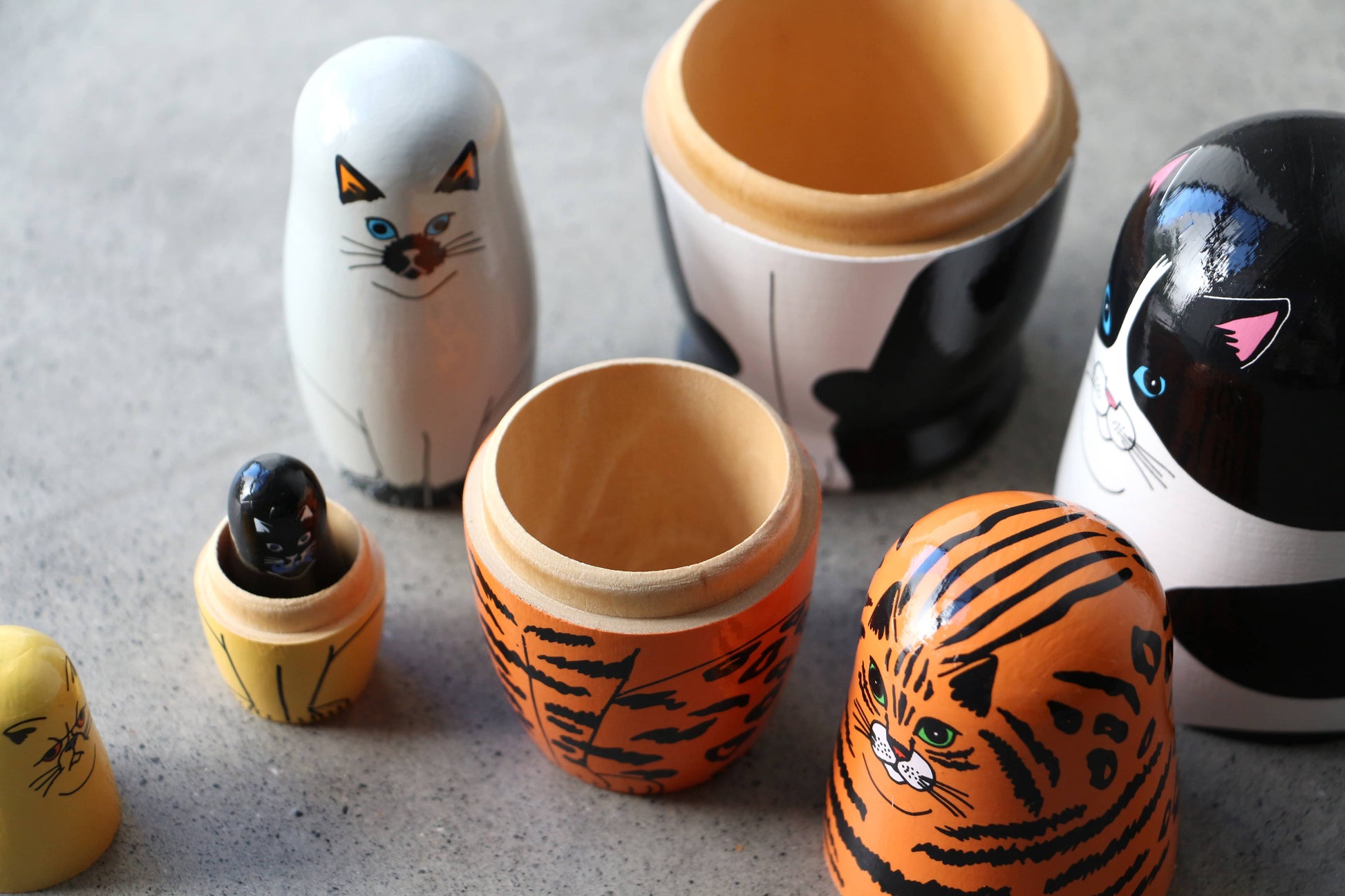 DETAIL Feline 5 Nesting Dolls by DETAIL, painted as a tiger, black-and-white cat, and white cat, are opened on a gray surface to reveal the smaller wooden nesting dolls inside—perfect for cat lovers.