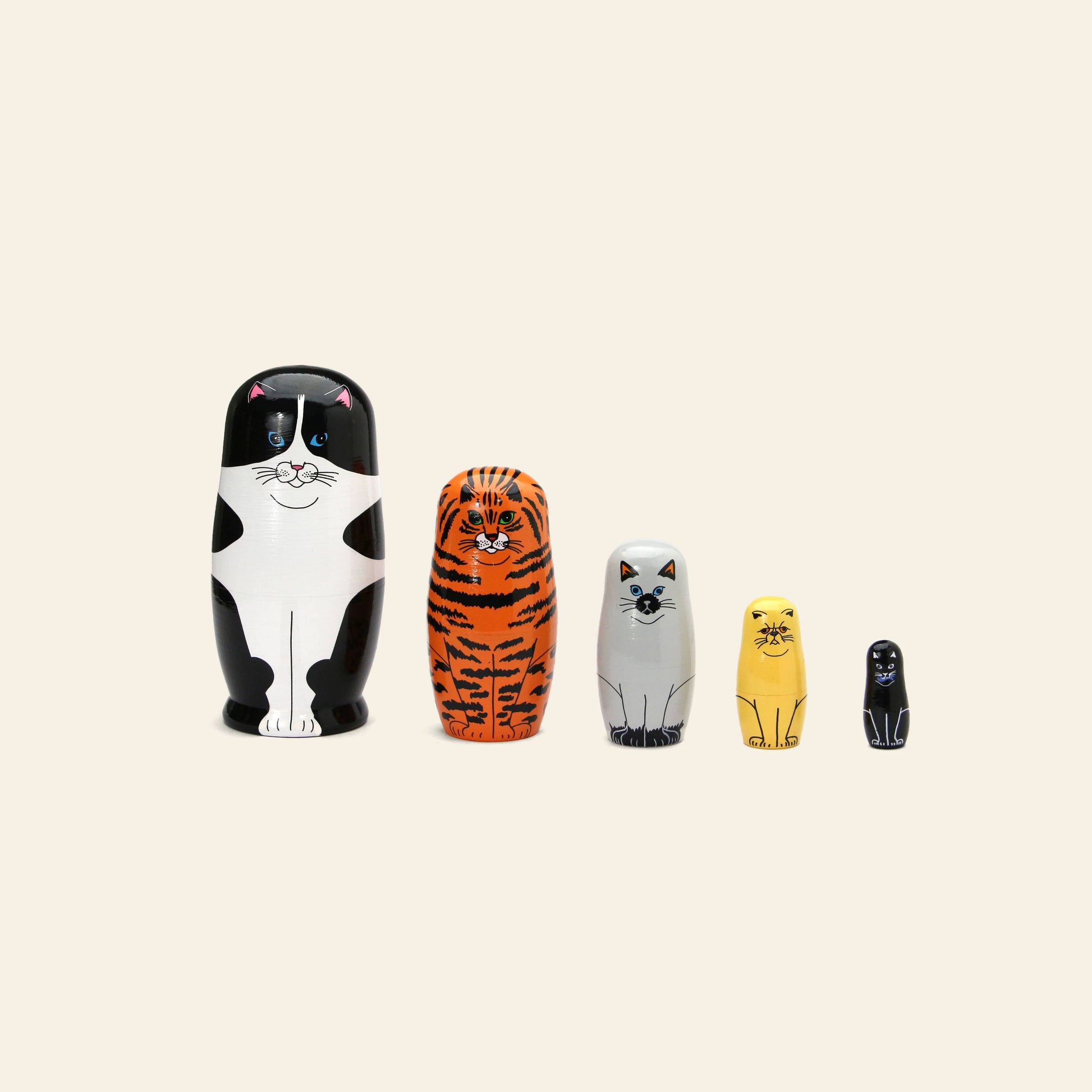 The DETAIL Feline 5 Nesting Dolls by DETAIL feature five wooden dolls of different sizes, each painted as a unique cat—ideal for cat lovers—arranged in a row on a plain beige background.