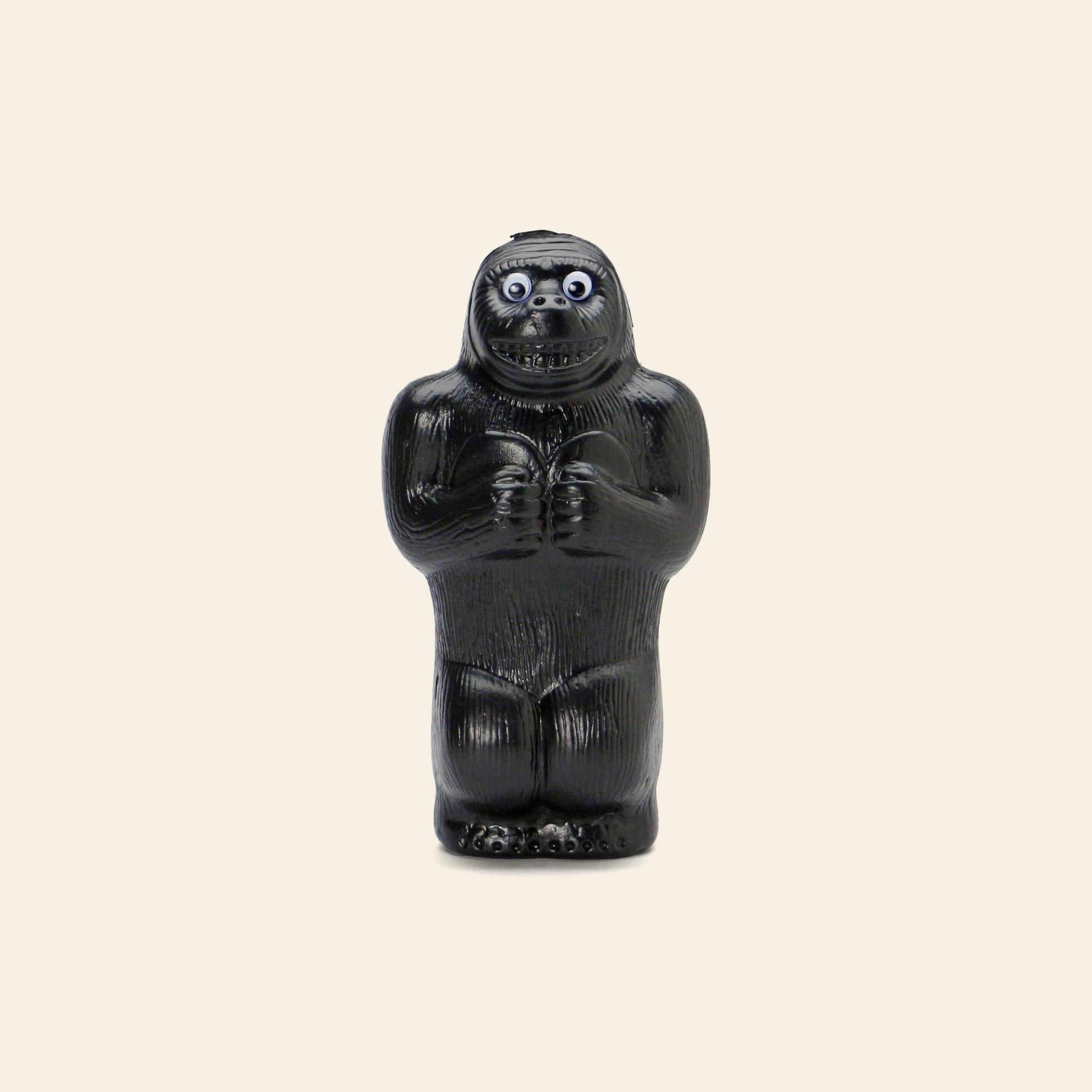 The DETAIL Gorilla Bank Small by DETAIL stands upright against a plain beige background, its wide eyes and slightly anxious expression making it a quirky decorative piece.