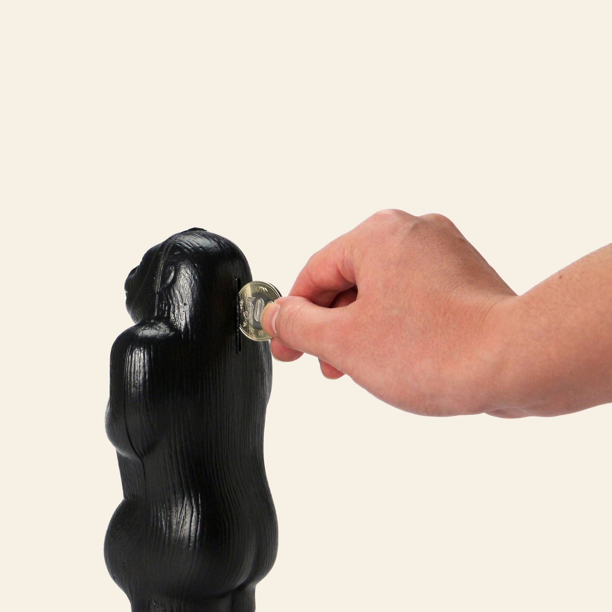 A hand inserts a silver key into the back of the DETAIL Gorilla Bank Small by DETAIL, a black figurine perfect as decor, set against a plain light background.