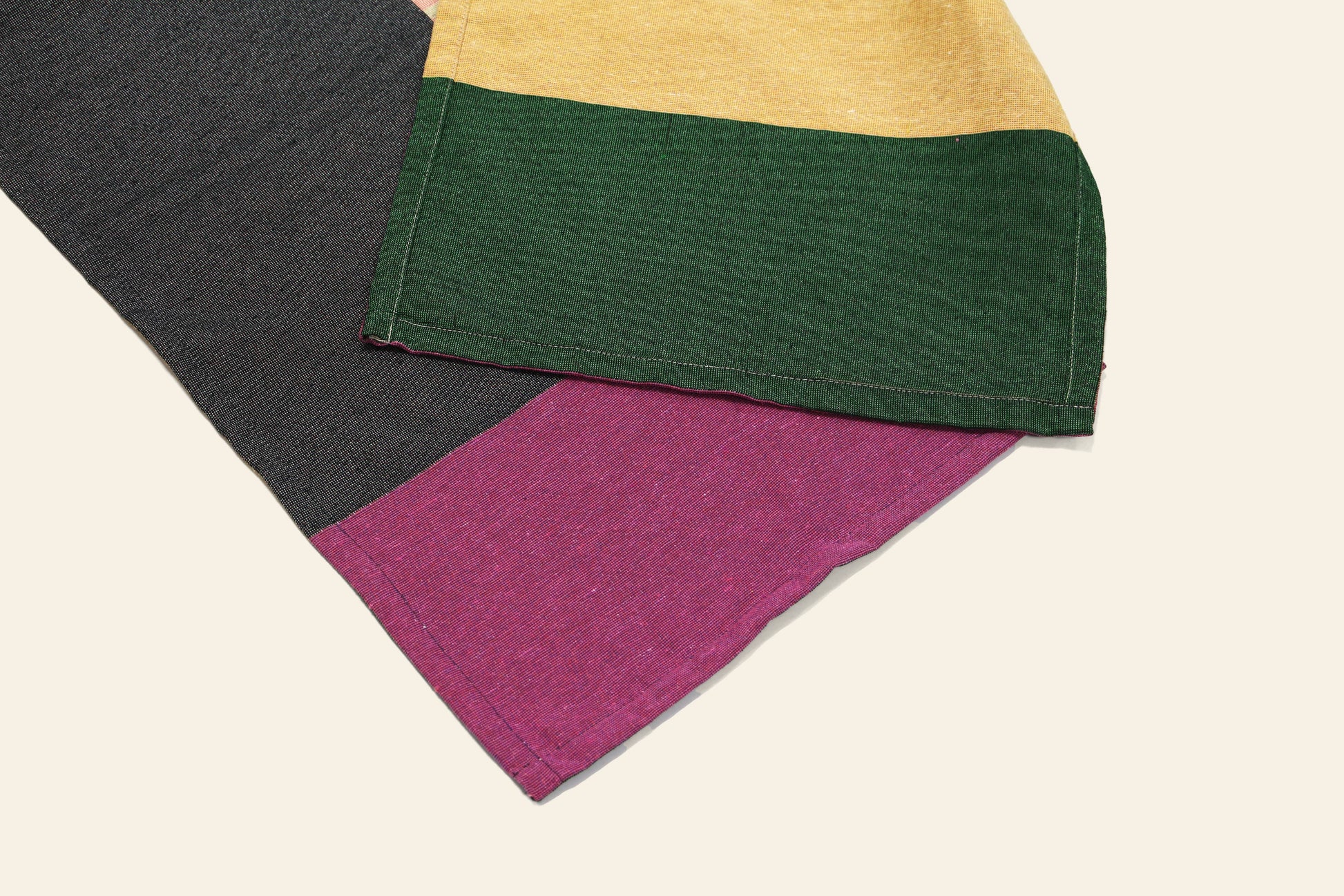 A close-up of the DETAIL Noren Curtain by DETAIL shows dark gray, purple, green, and yellow color blocks stitched in a plant-inspired design, reminiscent of traditional kimono patterns, displayed on a light background.