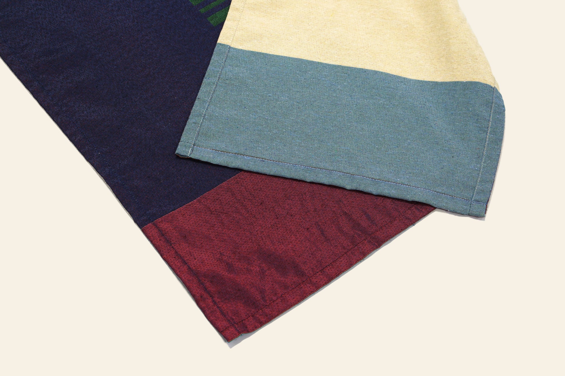The DETAIL Noren Curtain by DETAIL features overlapping fabrics—one in red and dark blue, the other in yellow and light blue with kimono-inspired patterns—set on a plain off-white background.