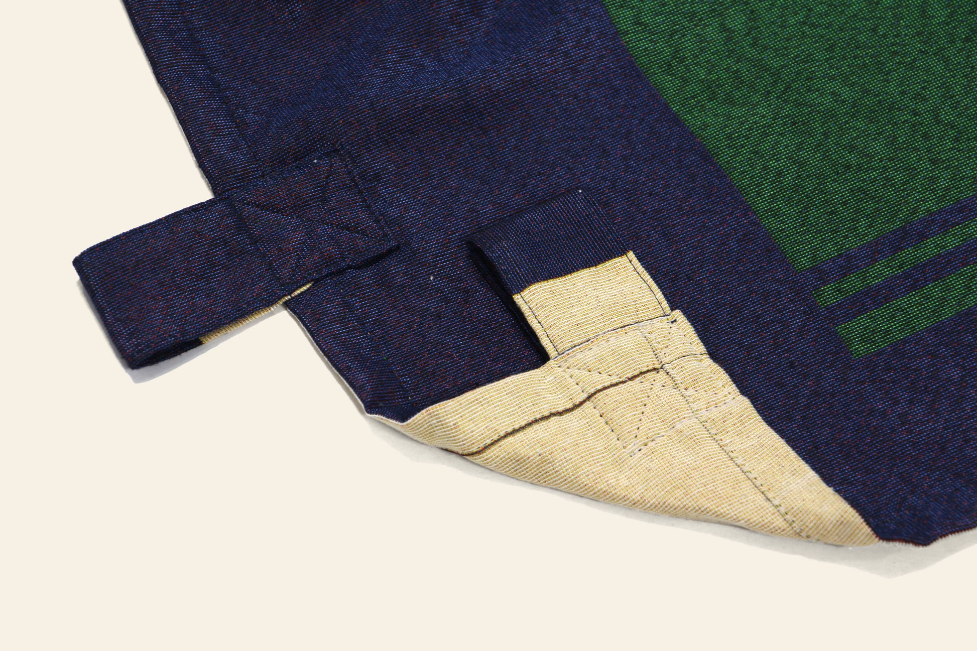 Close-up of the DETAIL Noren Curtain by DETAIL, highlighting its dark blue fabric, green-beige underside, reinforced stitched loop for hanging, and subtle kimono-inspired patterns.