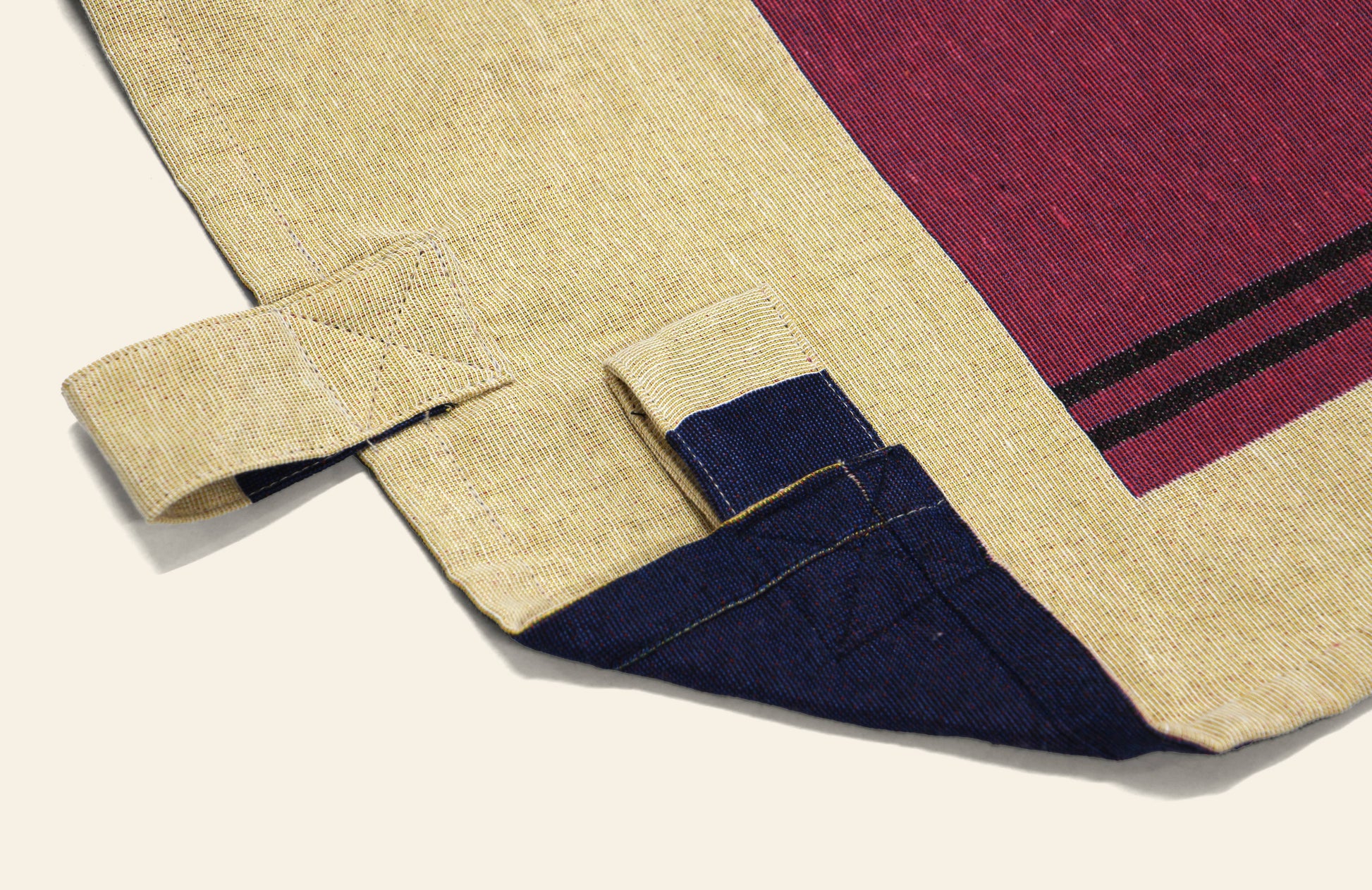 A close-up of the DETAIL Noren Curtain by DETAIL, showcasing a plant-inspired beige fabric with red and blue accents and two side loops, set against an off-white background.