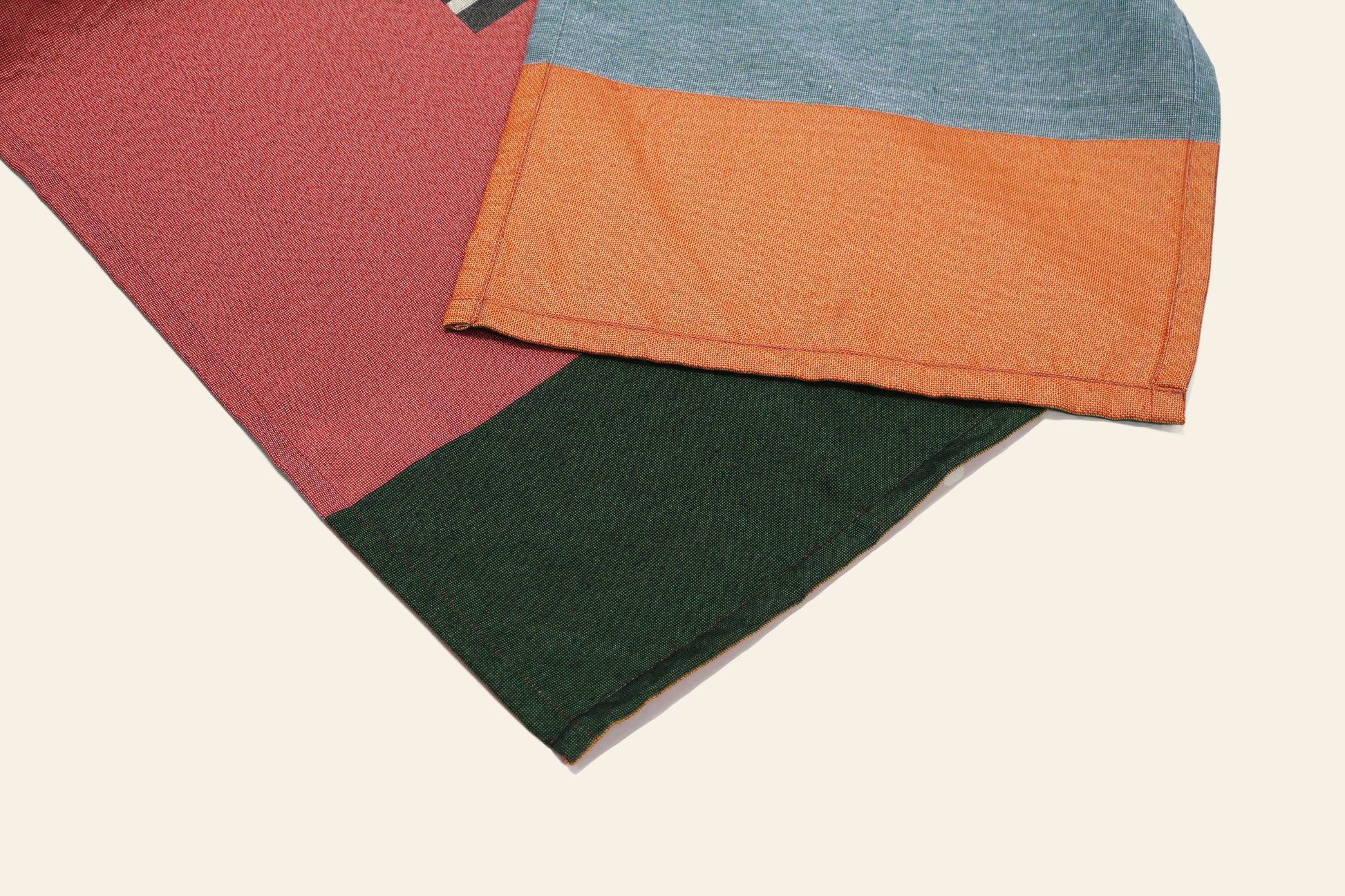 Two pieces of fabric from the DETAIL Noren Curtain by DETAIL overlap: one showcases blue and orange kimono patterns, the other has red and green sections. Both are set against a light background.