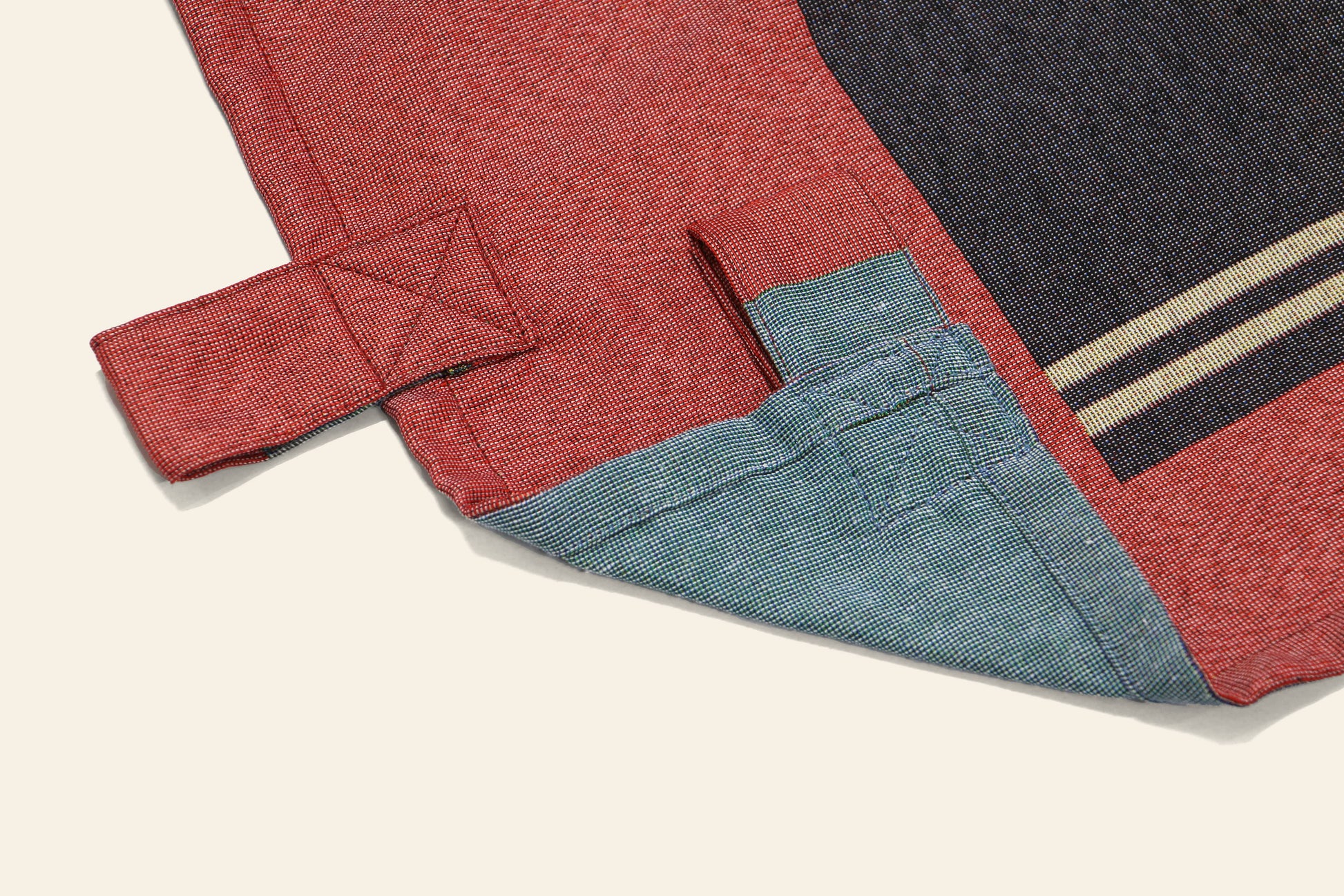 A close-up of the corner of the DETAIL Noren Curtain by DETAIL, featuring a stitched tab, folded hem with visible stitching, and a striped detail inspired by traditional kimono patterns in red and blue fabric.