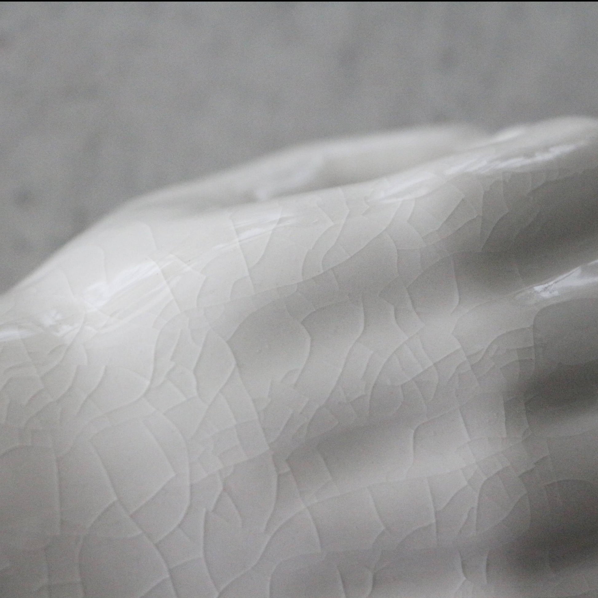 A close-up of the DETAIL Porcelain Hand Peace by DETAIL, a white, glossy accessory stand with a crackled texture, showcased against a soft-focus grey background.