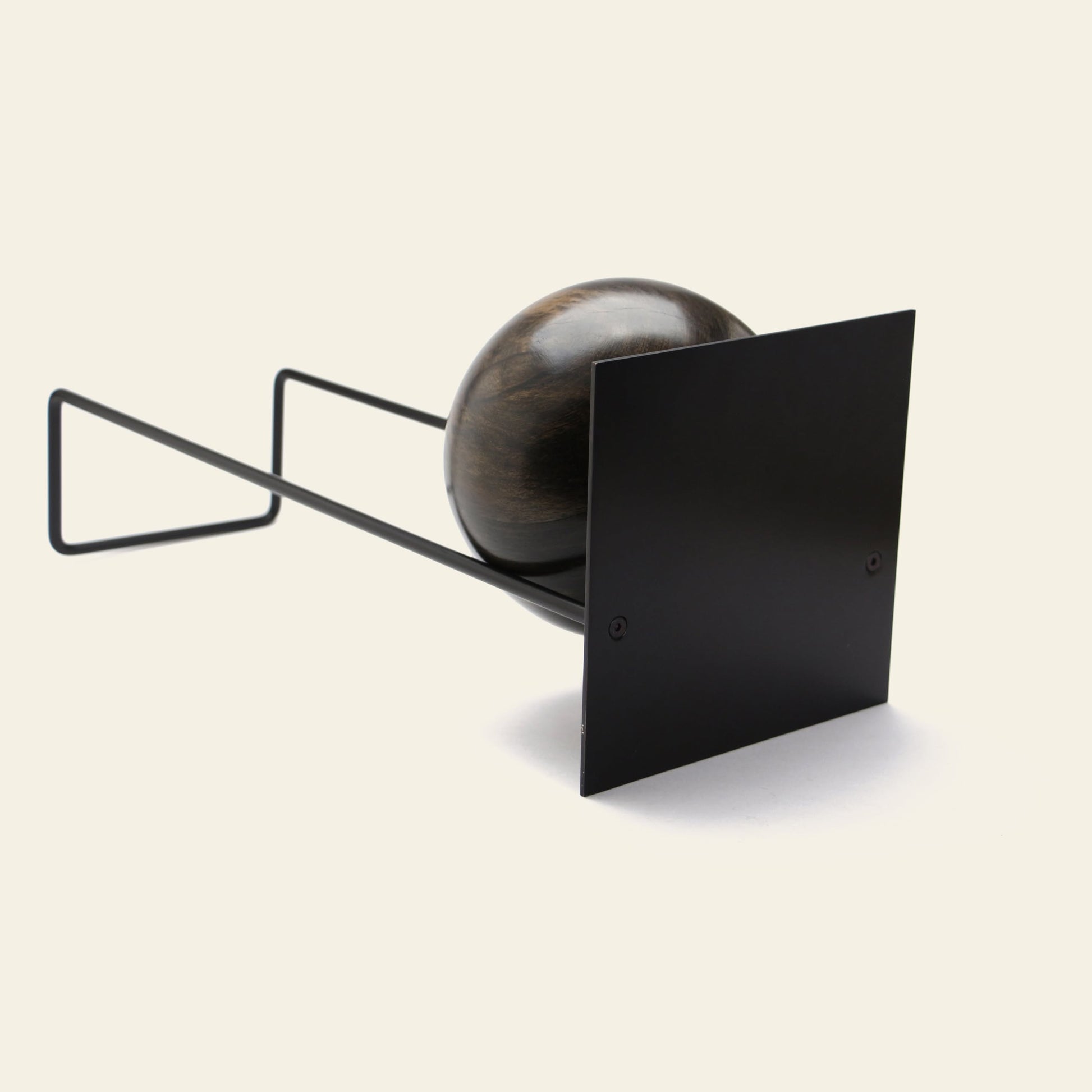 The DETAIL Slope Bookend by DETAIL features a dark wooden sphere partially covered by a black metal square, supported by a minimalist wire frame, set against a plain light background.