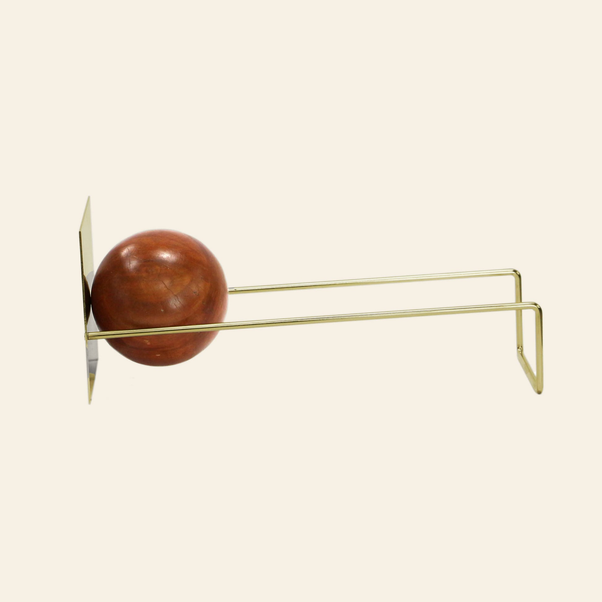 The DETAIL Slope Bookend by DETAIL features a minimalist design of brass and wood, with a unique mango wood ball accent on parallel brass rods—perfect for organizing books. Its modern style stands out against a cream background.