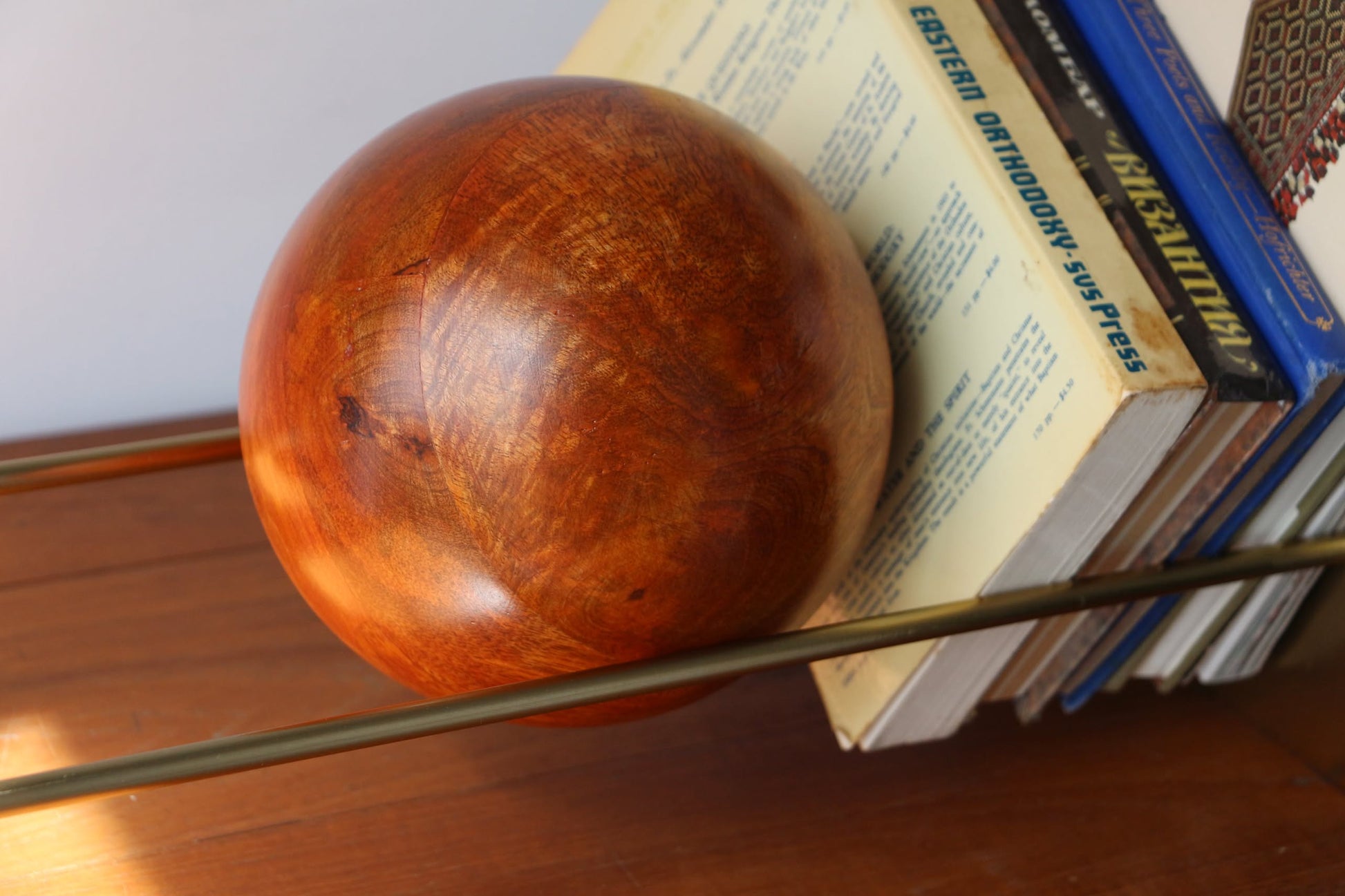 The DETAIL Slope Bookend by DETAIL features gold-colored rods and a mango wood ball, supporting upright books with visible titles on a wooden surface, bringing minimalist design to your space.