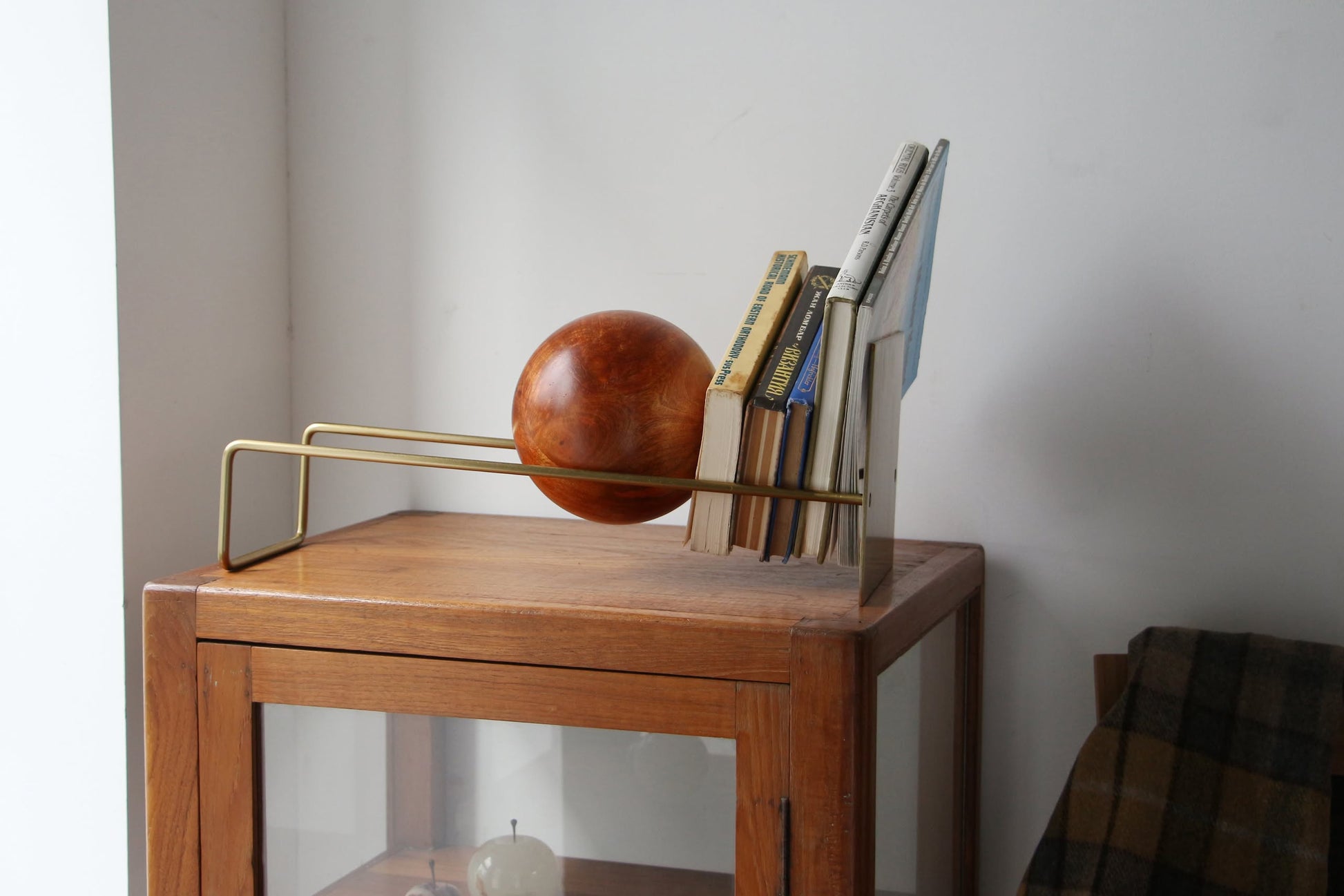 The DETAIL Slope Bookend by DETAIL features a unique mango wood ball and minimalist design, supporting several books atop a wooden cabinet against a plain white wall.