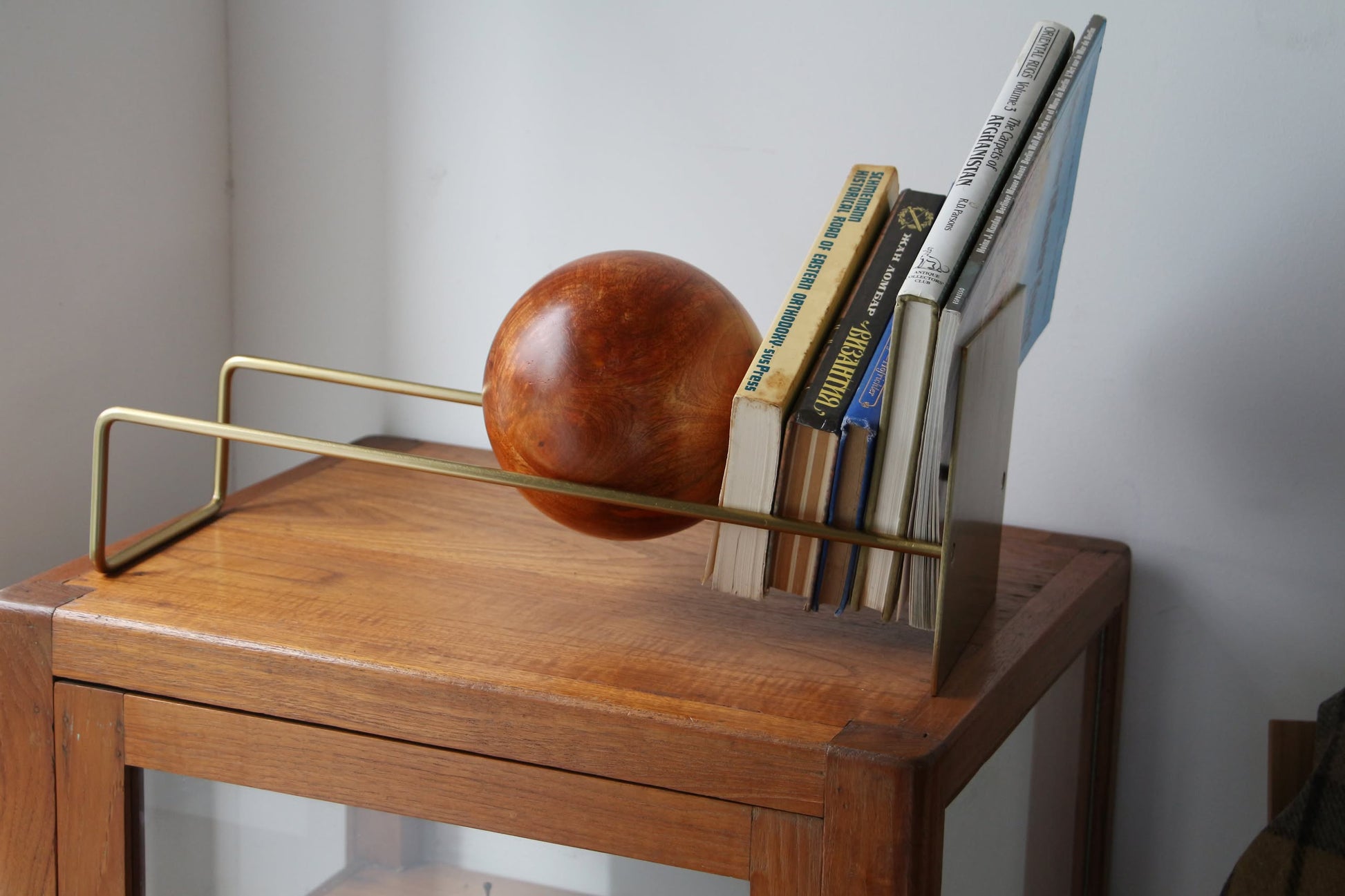 The DETAIL Slope Bookend by DETAIL features a unique mango wood ball, blending brass and wood in a minimalist design to elegantly support books on any wooden cabinet.