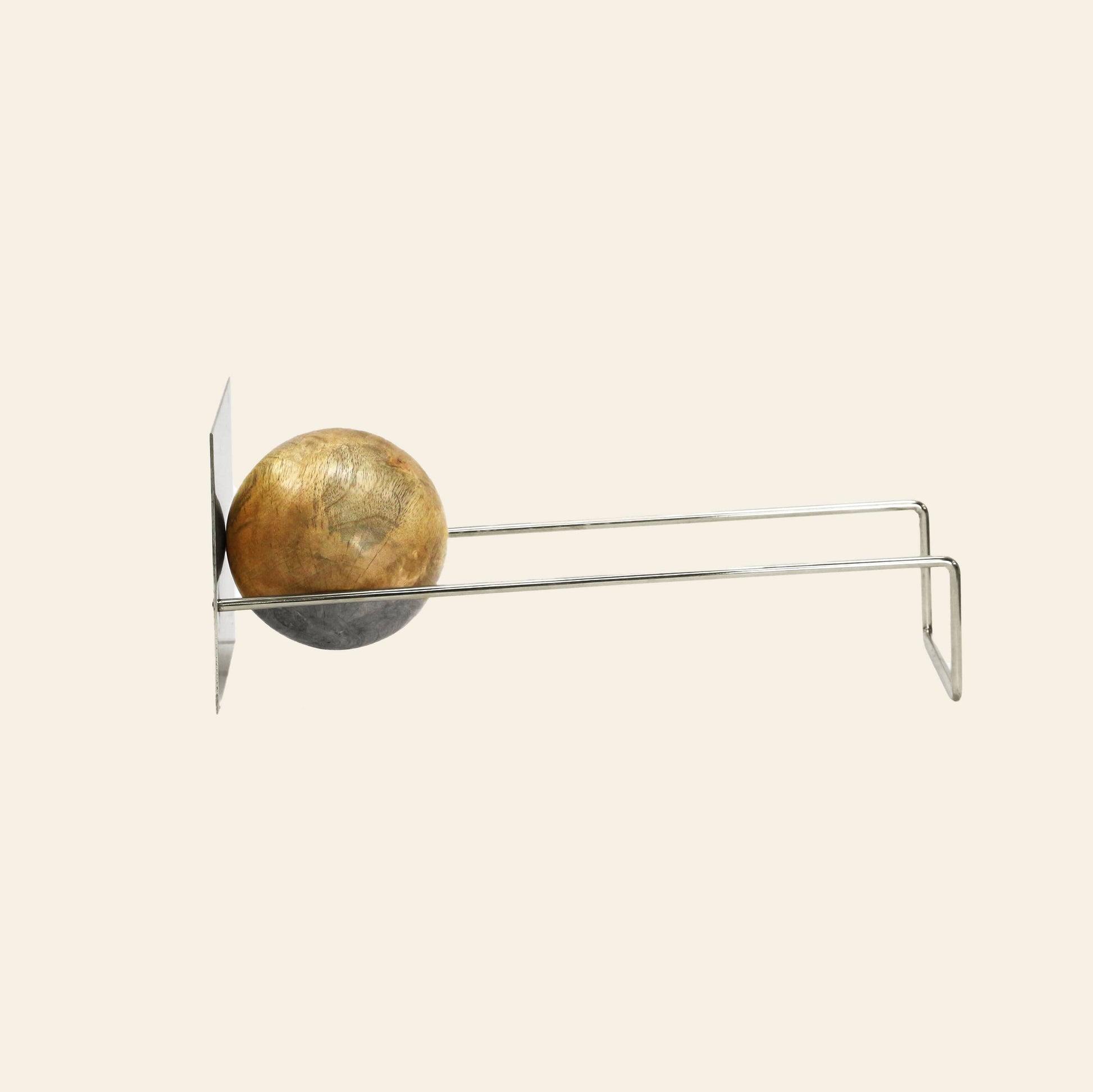 A DETAIL Slope Bookend by DETAIL, featuring a unique mango wood ball, supports several books on top of a wooden cabinet with glass doors. Inside the cabinet are decorative objects, including two small apple-shaped items.