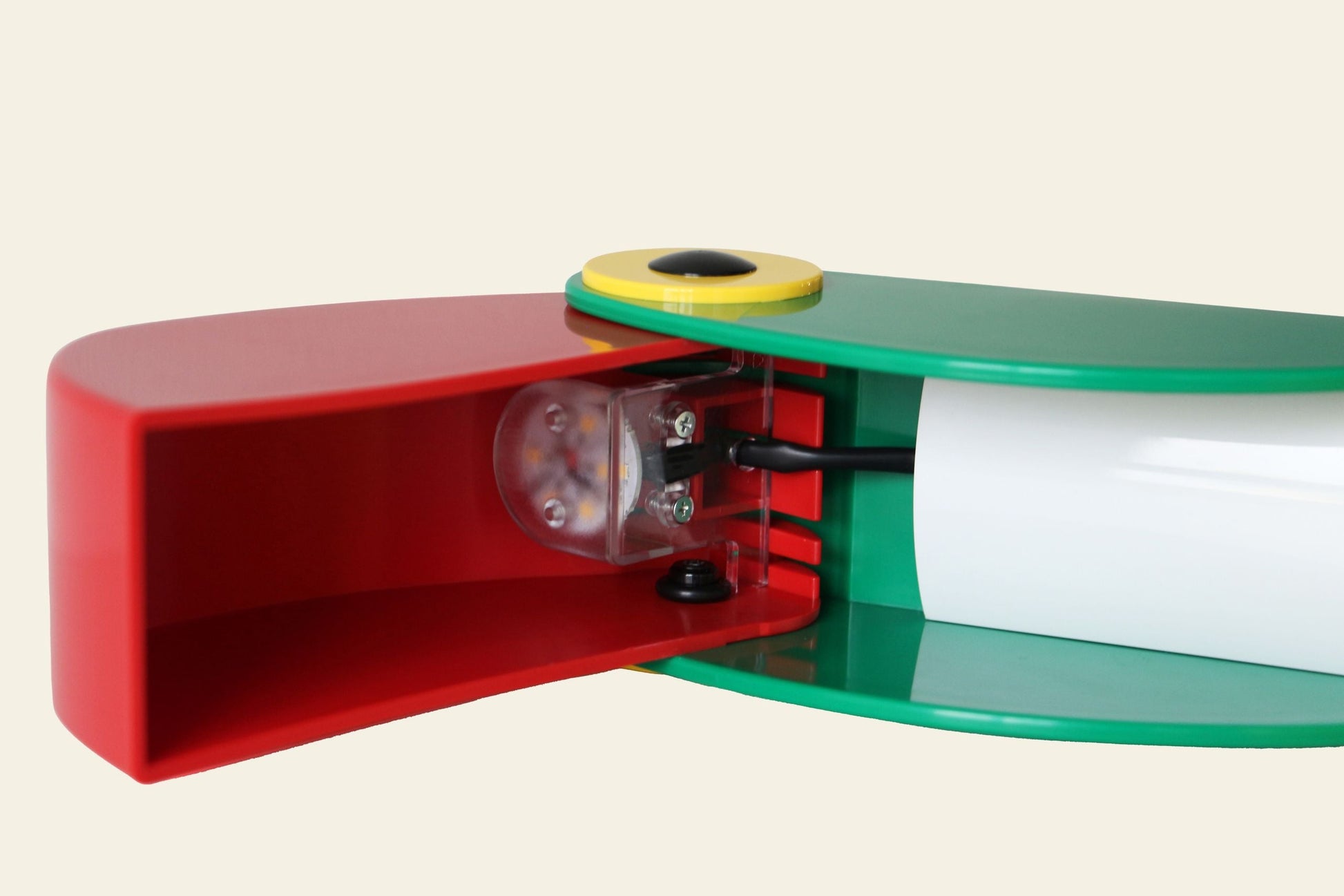 Close-up of the DETAIL Toucan Lamp by DETAIL, featuring colorful red and green panels, a yellow circular accent, and exposed internal electronics—showcasing iconic vintage-inspired design against an off-white background.