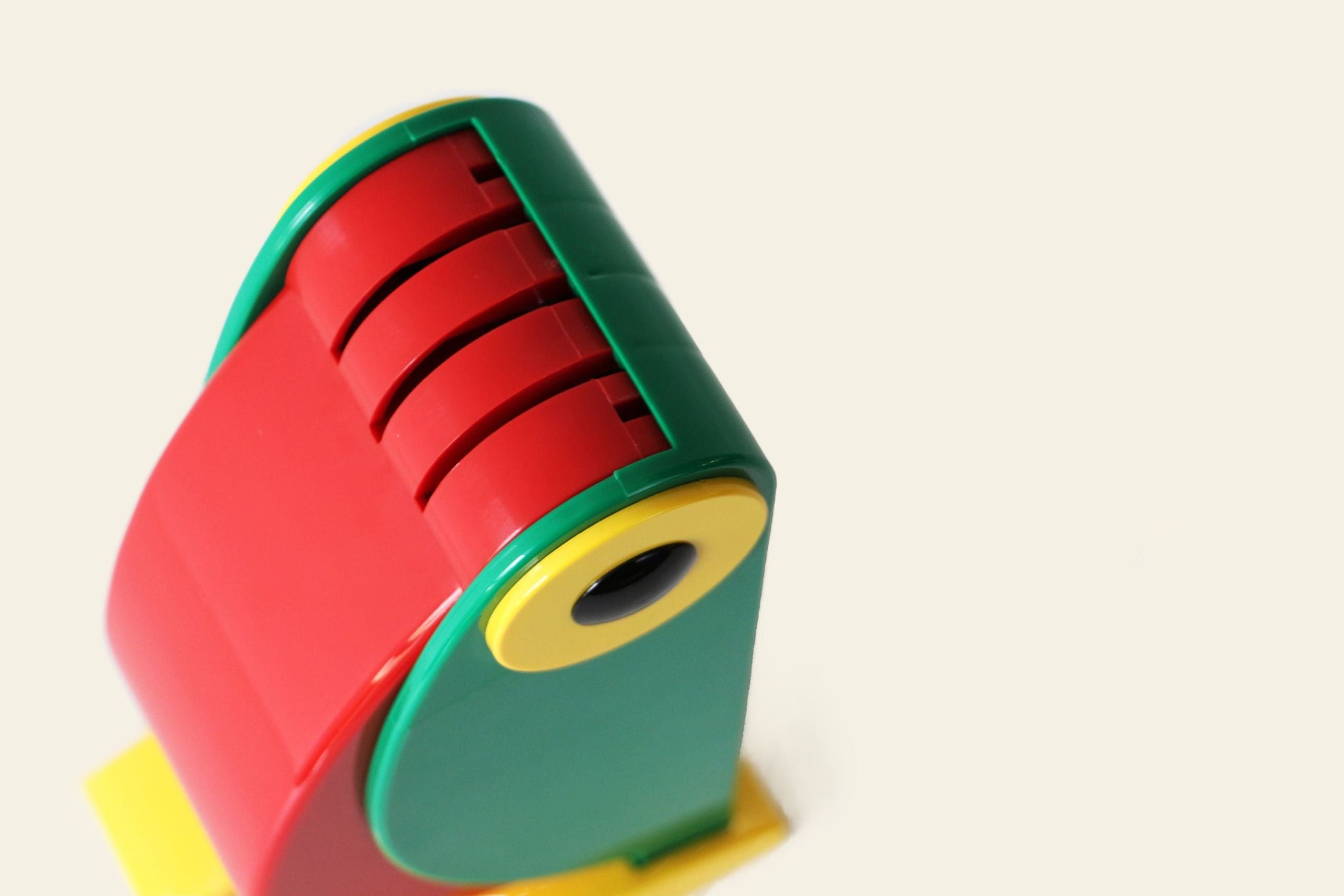 The DETAIL Toucan Lamp by DETAIL is a colorful plastic piece with red, green, and yellow curved parts and red slots, photographed on a light background. Its vintage design hints at iconic style, though its exact purpose remains intriguing.