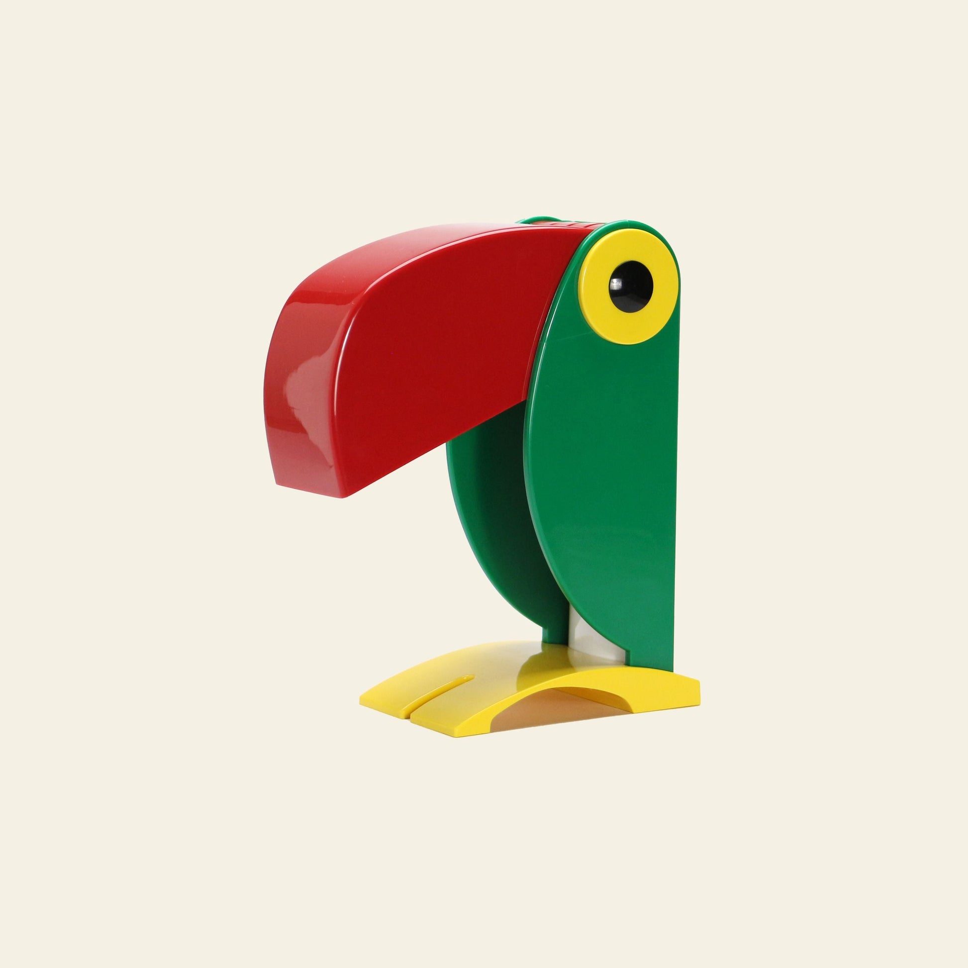 The DETAIL Toucan Lamp by DETAIL features a colorful, minimalist design with a large red beak, green body, yellow feet, and a yellow-rimmed eye, capturing iconic vintage charm against a plain light background.